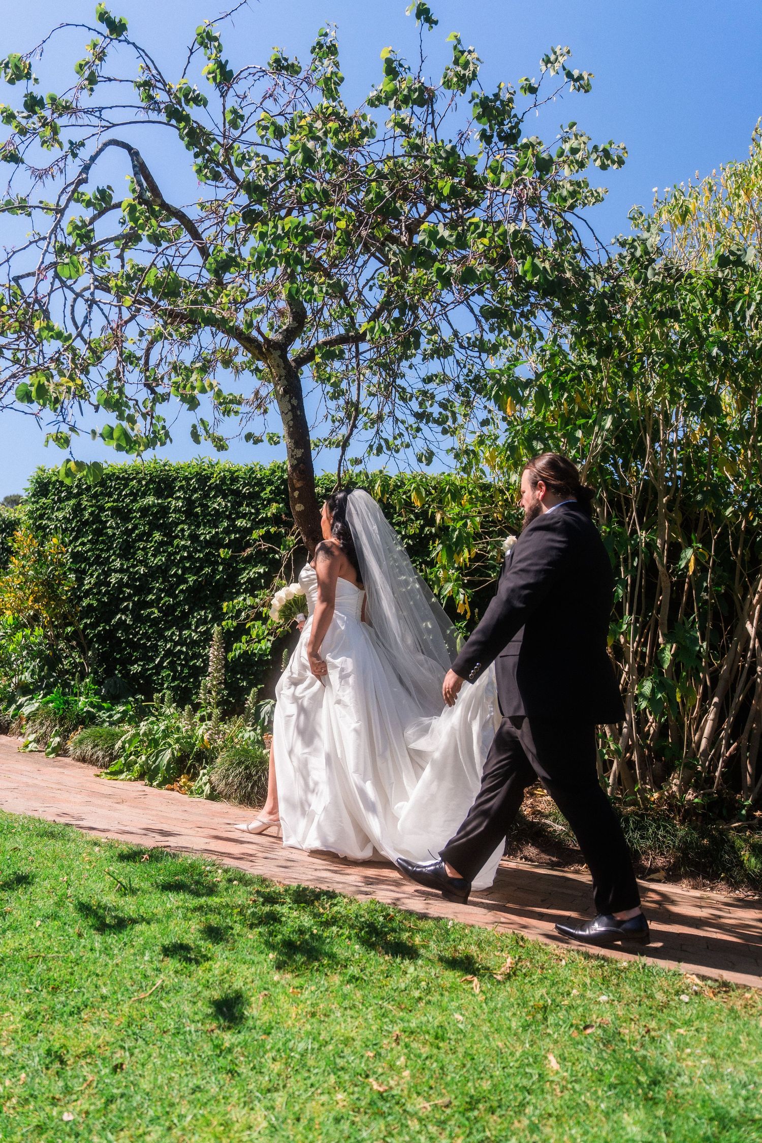 Wedding couple poses playfully on a grassy hill surrounded by lush greenery.