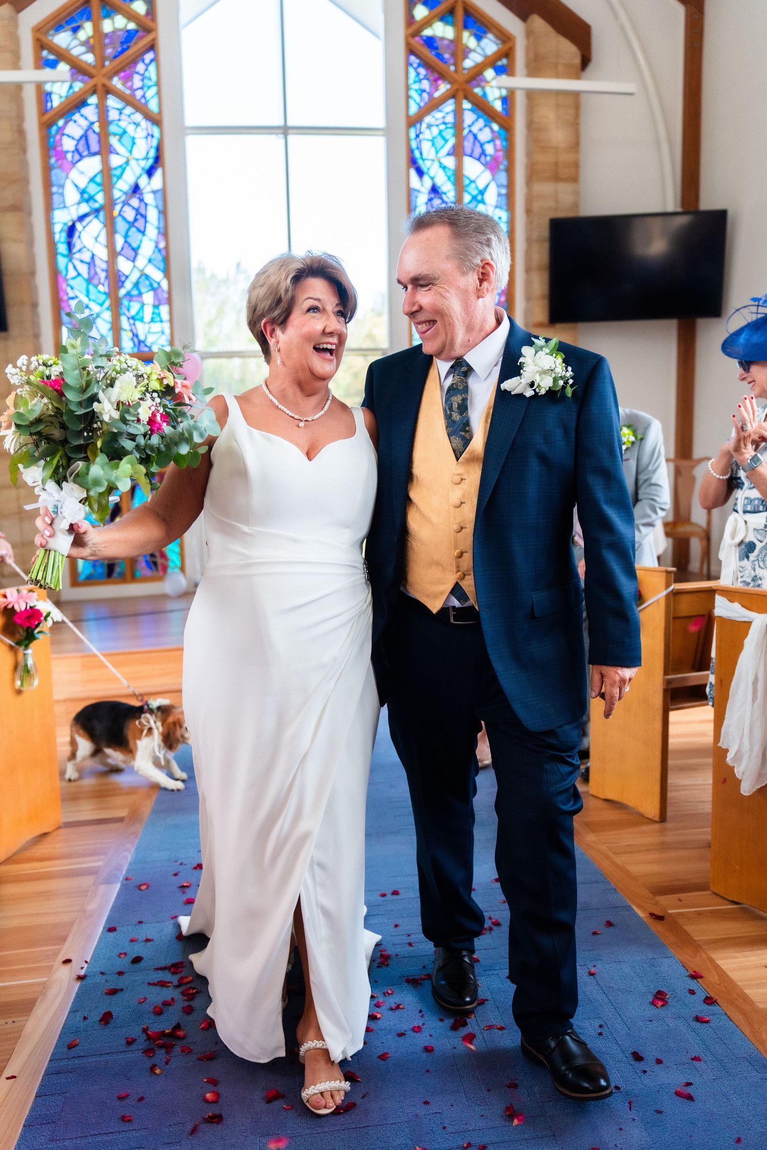 Couple walking down church aisle decorated with rose petals and stained glass windows.