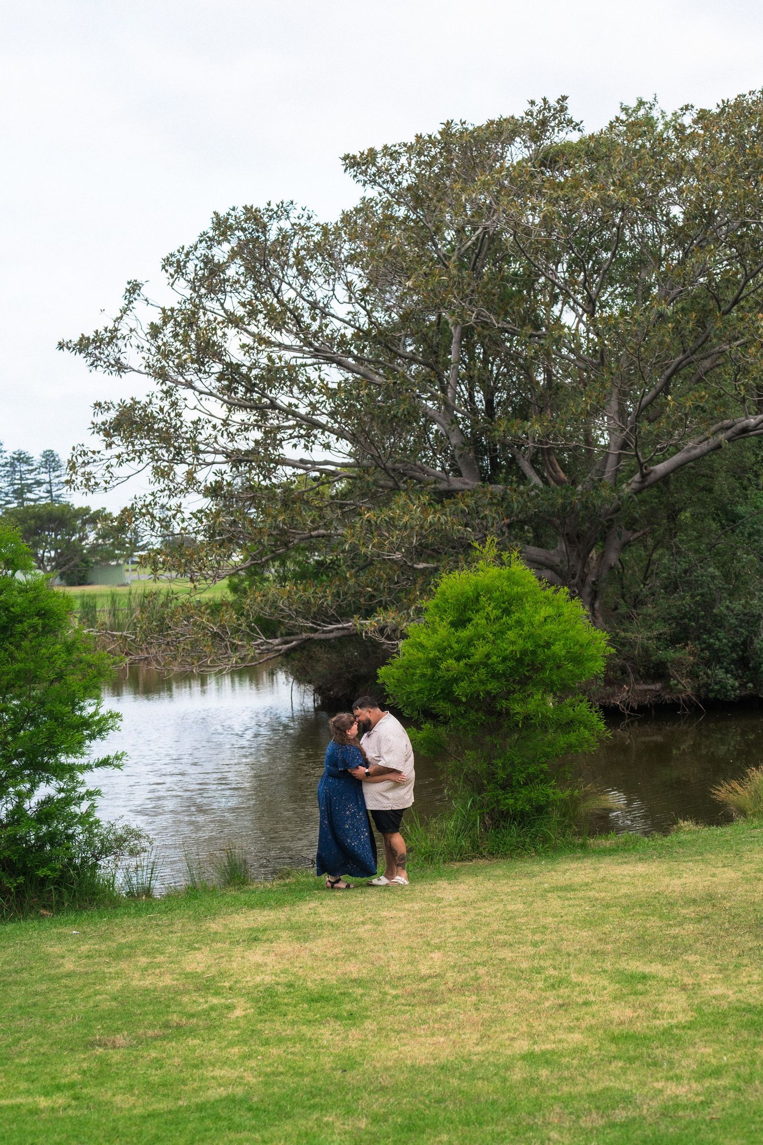 Romantic moment captured by a serene lake with overhanging trees framing the scene.