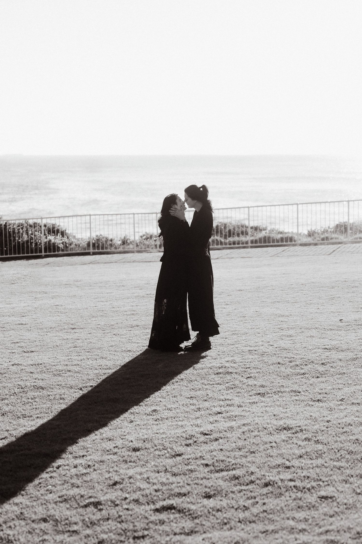 Black and white silhouettes of two people sitting together cast long shadows across an open field.