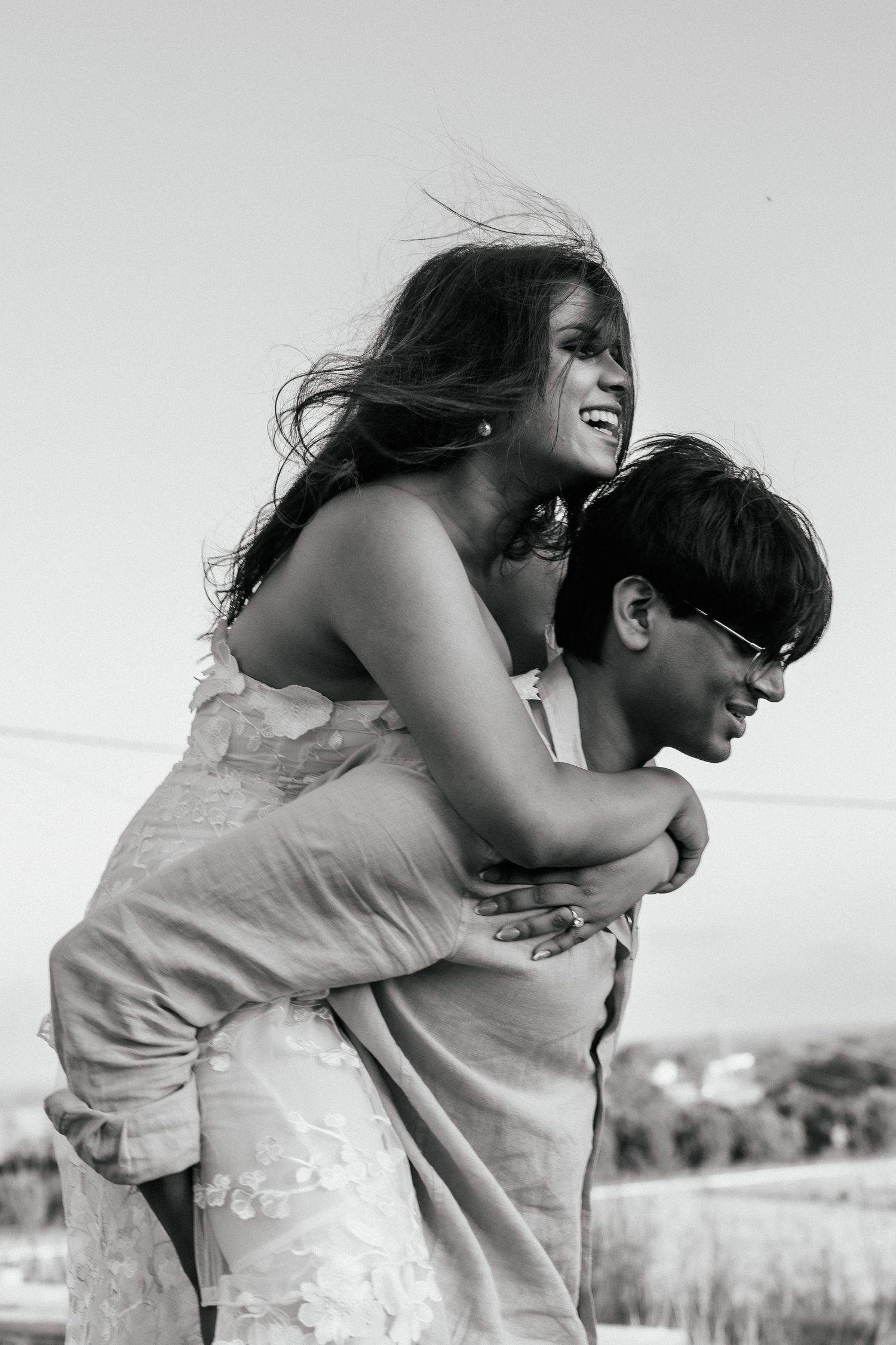 Black and white photo of a couple embracing outdoors in casual clothing.