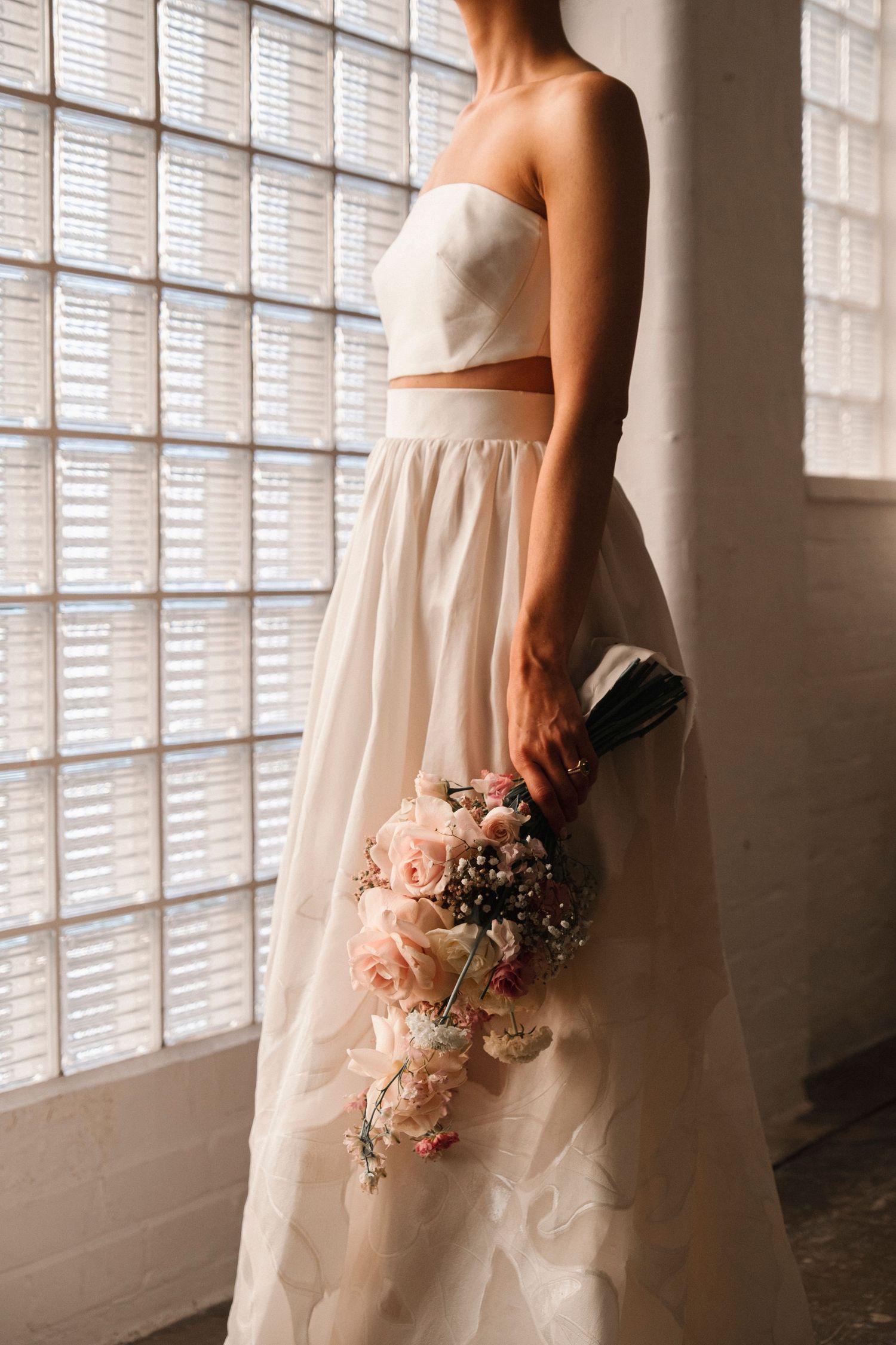 Elegant white wedding dress details with delicate bouquet against window light.