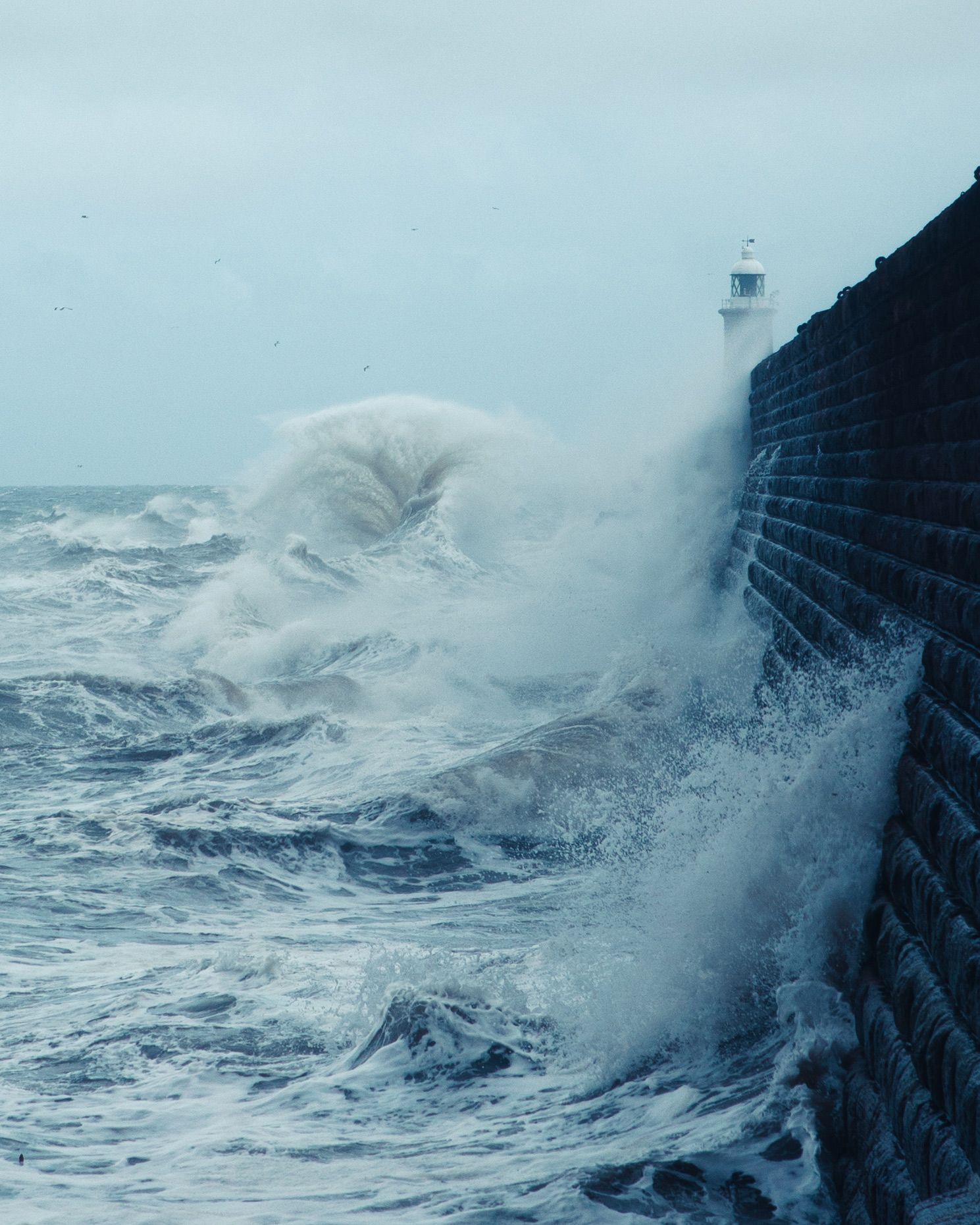Massive waves crash against dark coastal cliffs during a powerful storm.