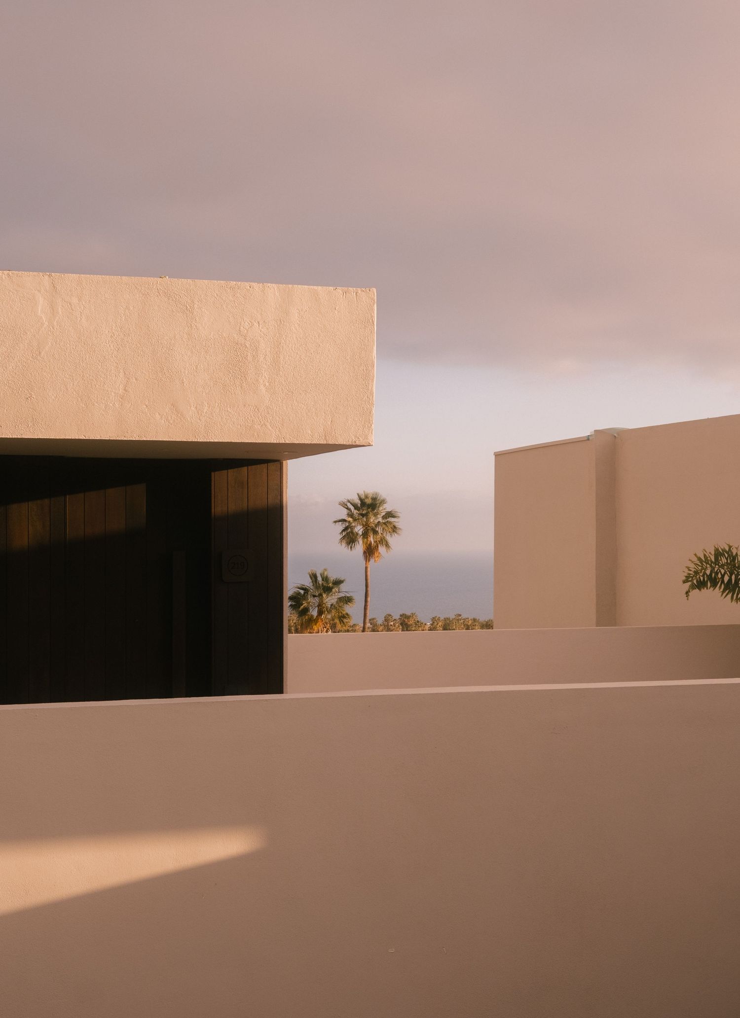 Minimalist beige stucco architecture with palm trees and a soft pastel sky in a warm desert setting.