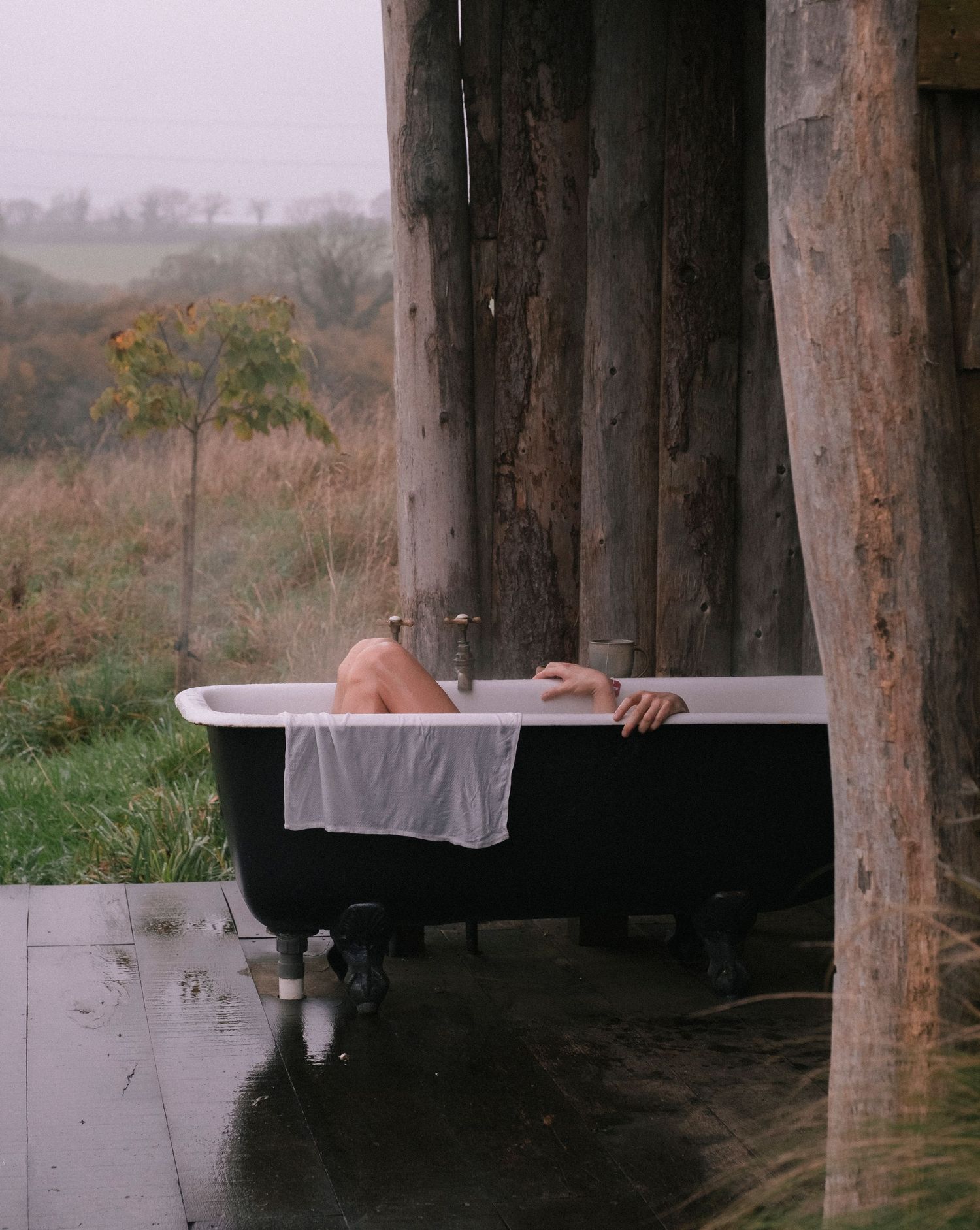 Vintage clawfoot bathtub on wooden deck overlooking misty countryside view.