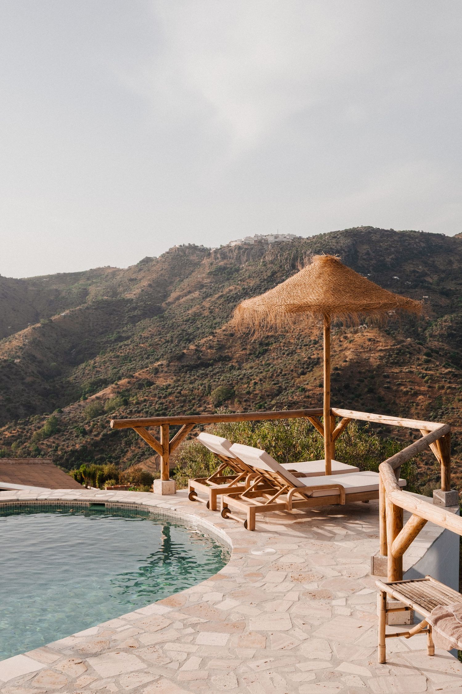 Infinity pool terrace with wooden loungers overlooking dramatic mountain landscape at sunset.