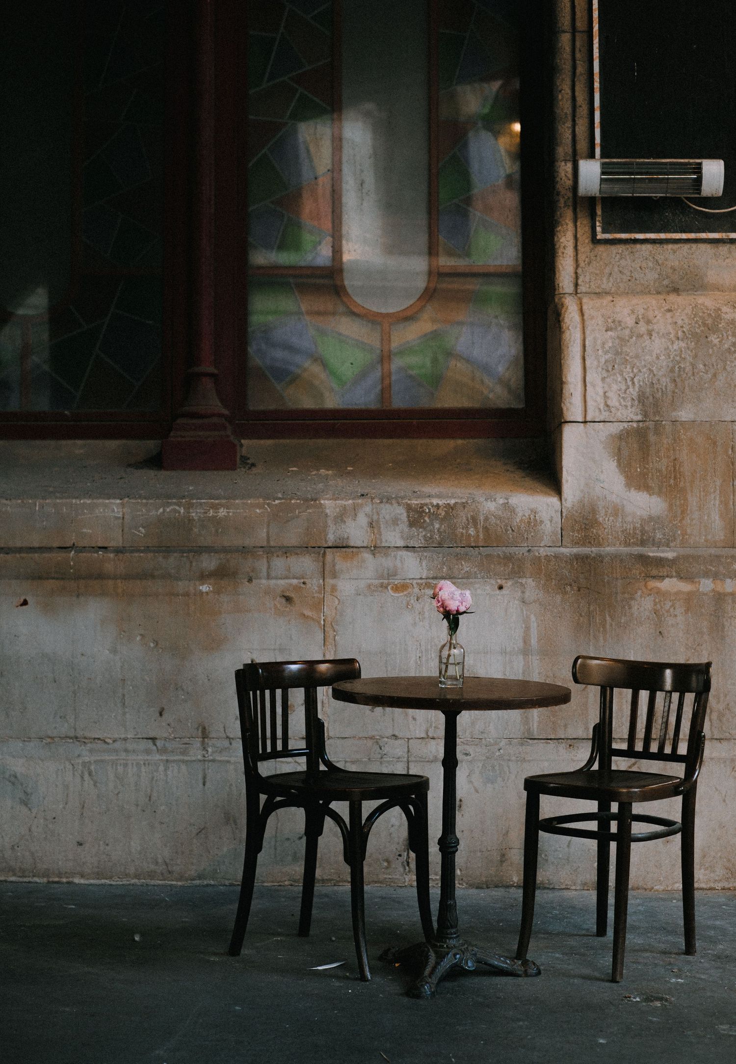 Dark moody cafe setting with vintage wooden chairs and round table against stone wall.