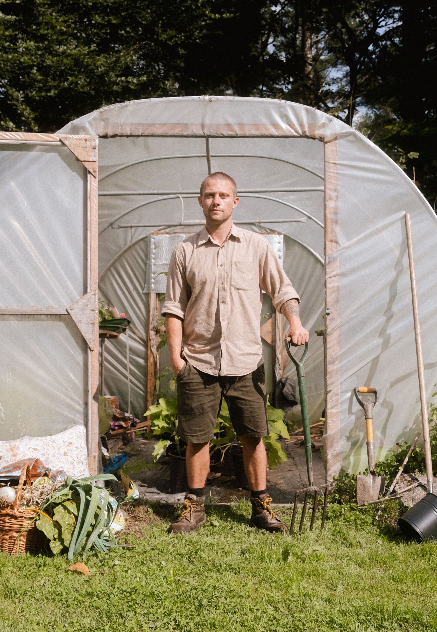Person in vintage clothing standing in front of greenhouse structures.