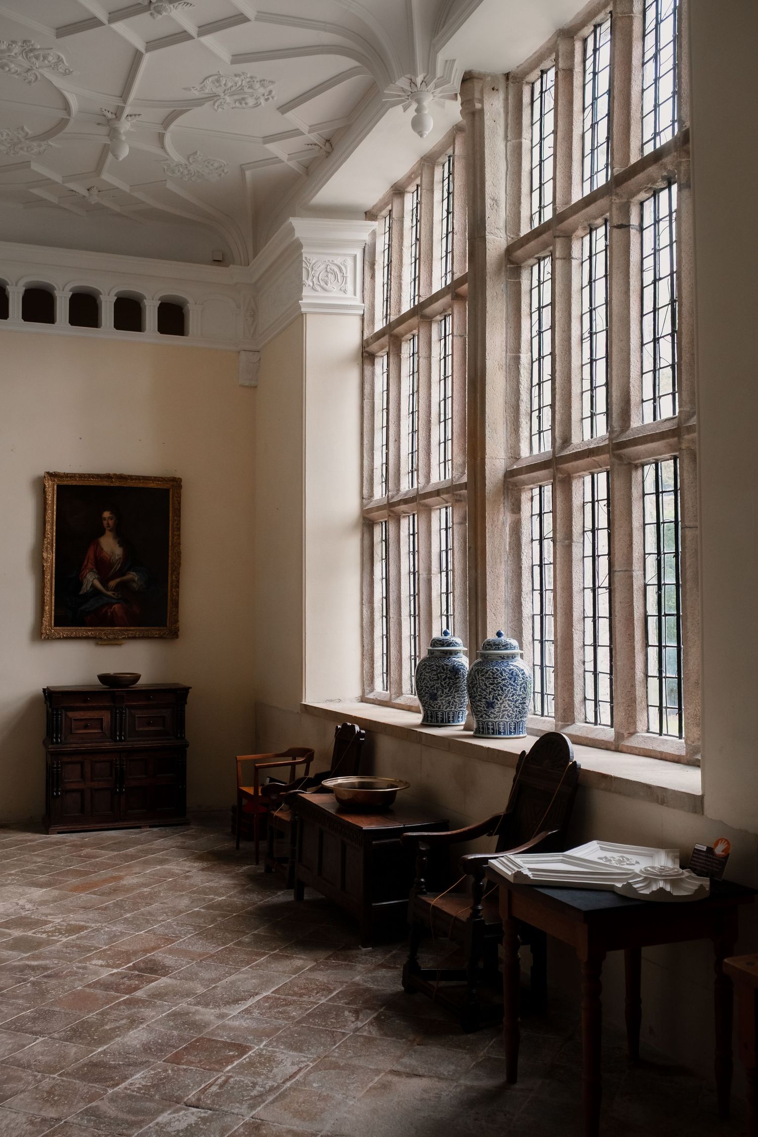 Historic room with ornate ceiling, tall windows, and antique furniture in natural light.