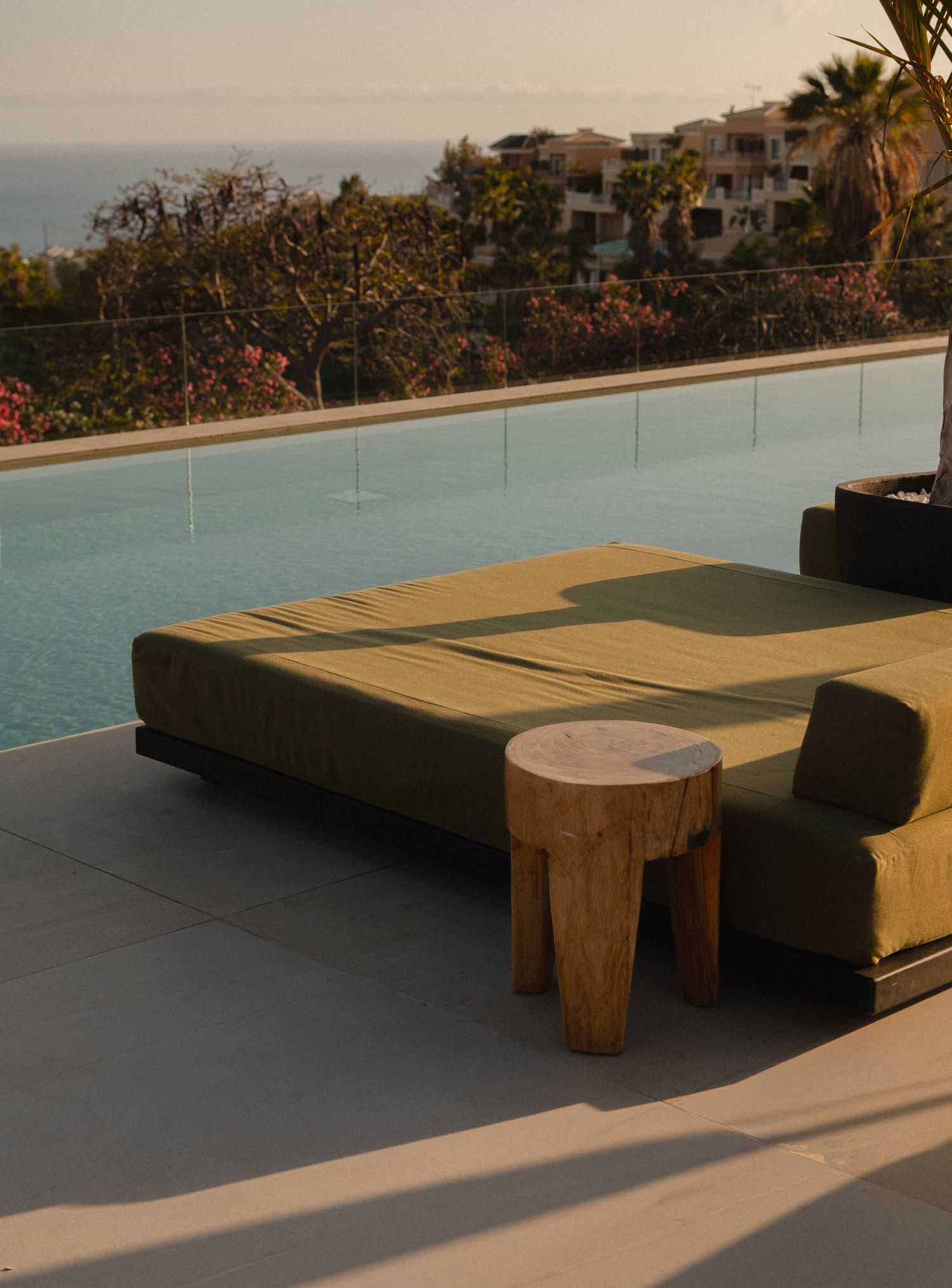 Luxury outdoor daybed with green cushion beside infinity pool overlooking Mediterranean hillside at golden hour.