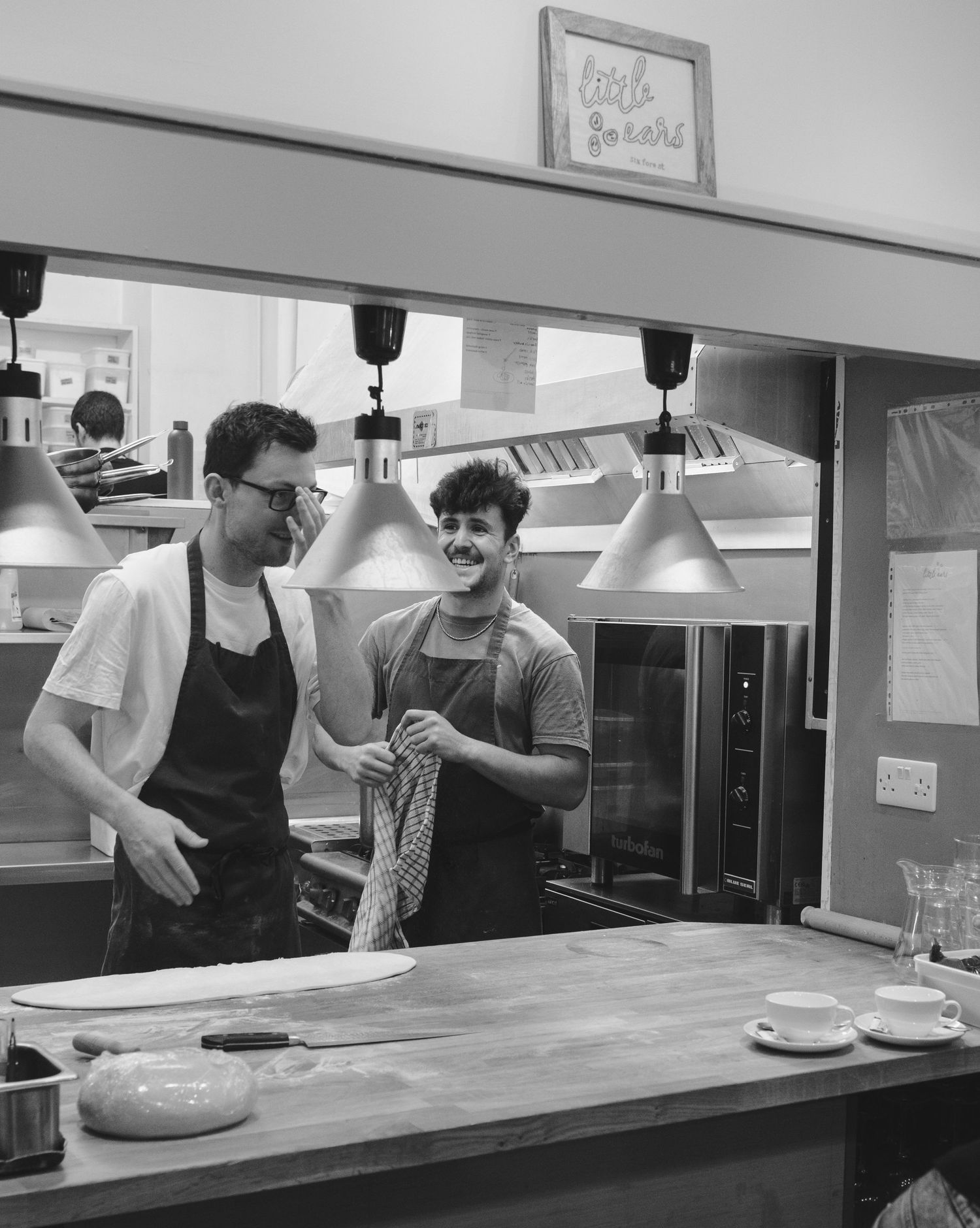 Black and white image of restaurant kitchen pass with chefs working.