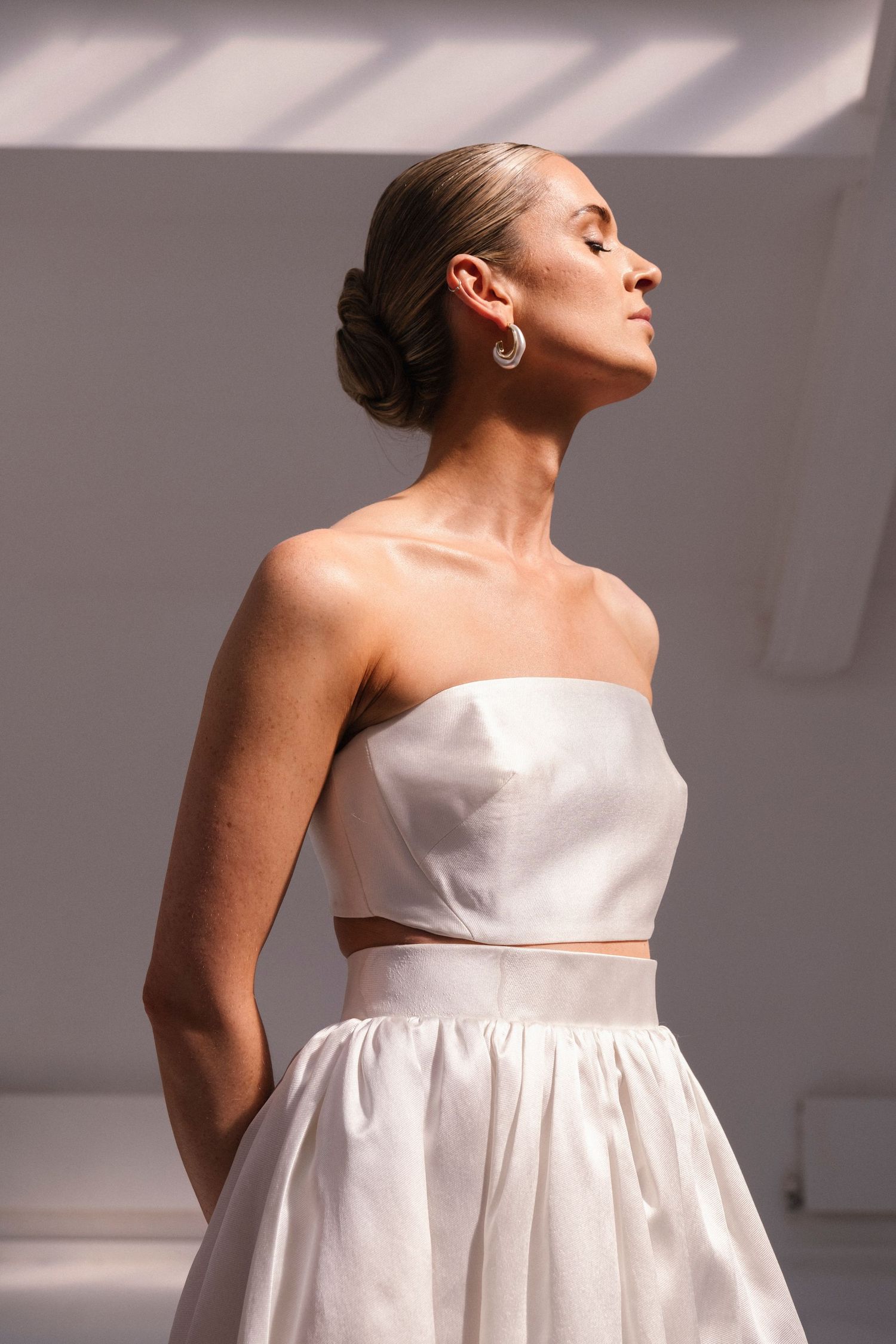 Minimalist bridal portraits in white dress against dramatic lighting.