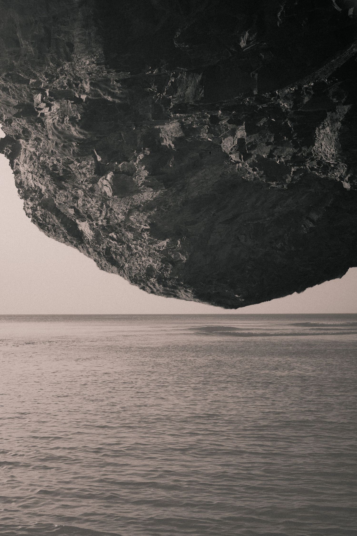 A series of minimalist black and white landscape photos showing dark cliffs against calm water with moody lighting.