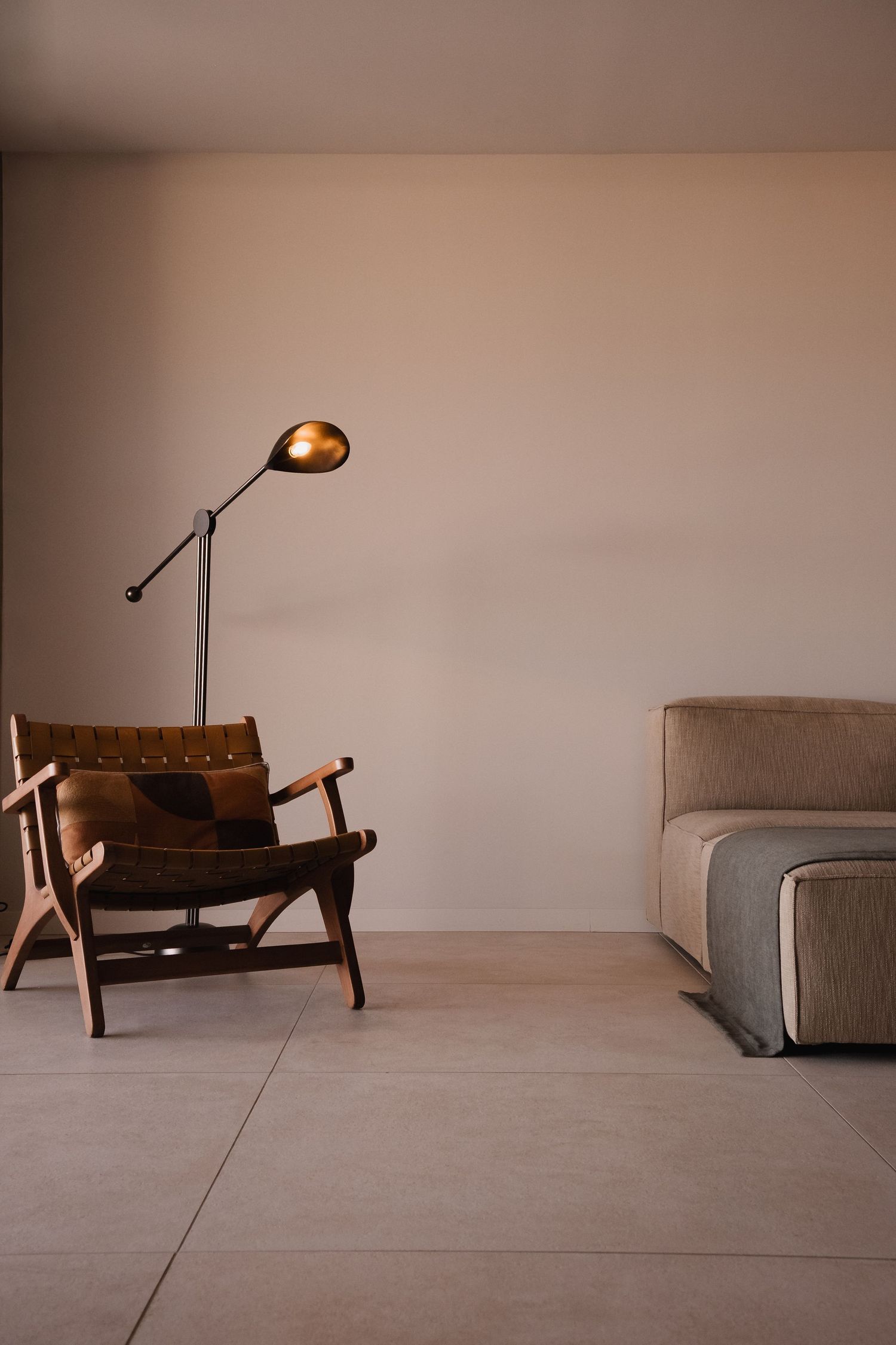 Minimalist living room with leather armchair, floor lamp, and beige sofa on light tile flooring.
