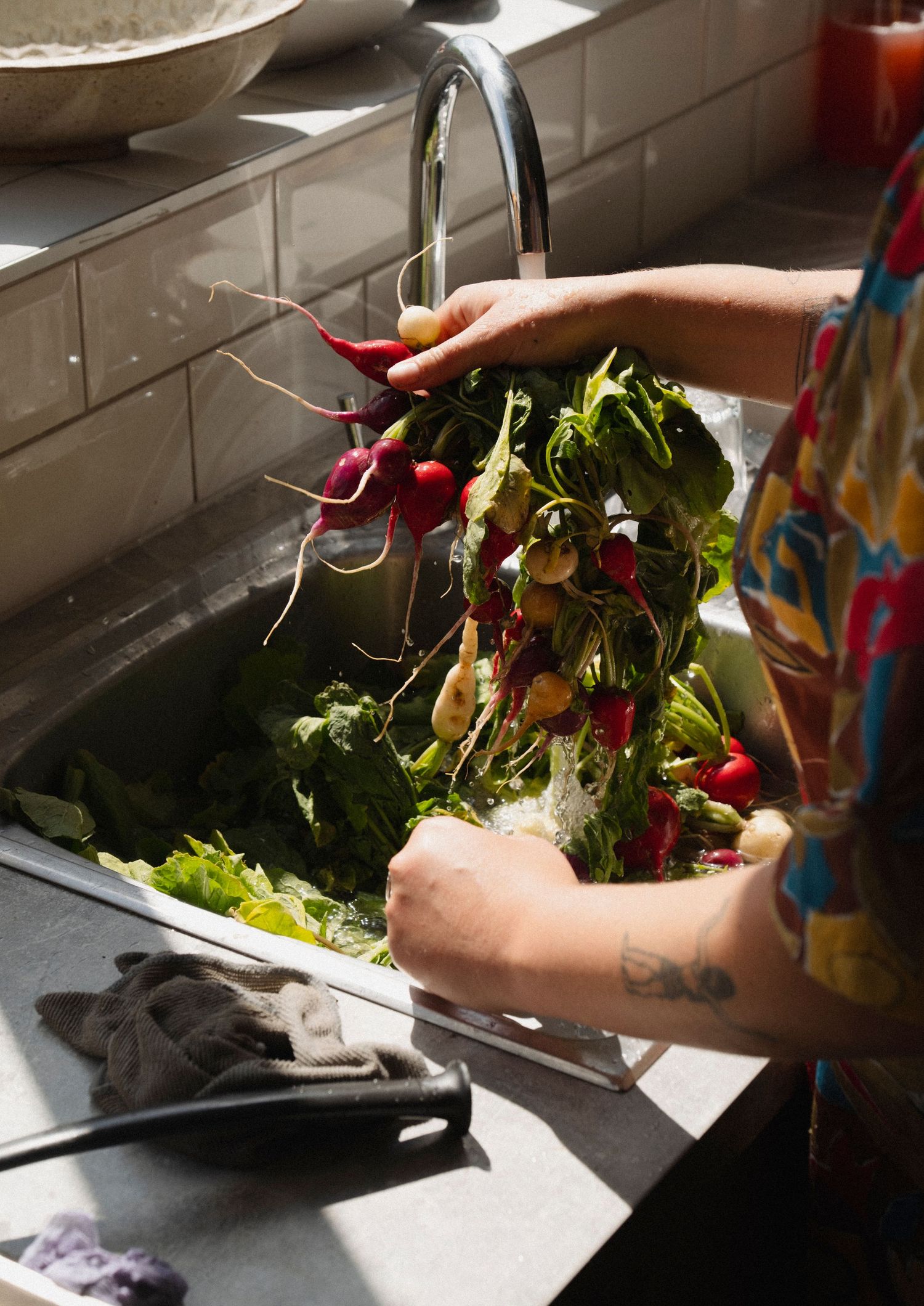 Hands washing fresh vegetables in a kitchen sink with running water.