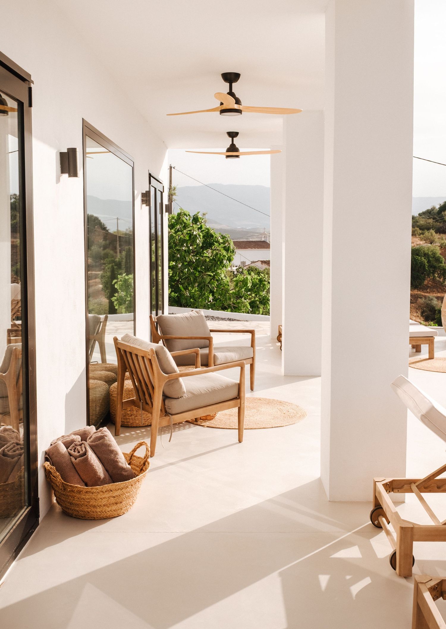 Sun-filled white terrace with wooden furniture and mountain views through large windows.