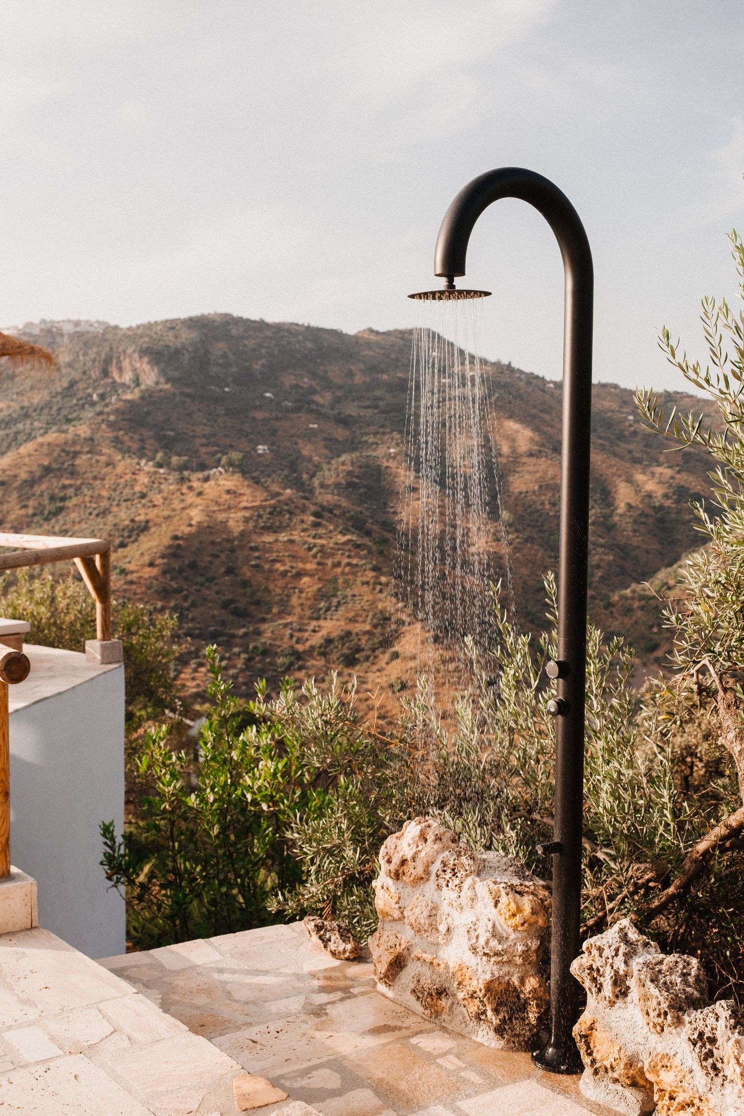 Modern outdoor shower with black fixtures against white walls overlooking mountain landscape.