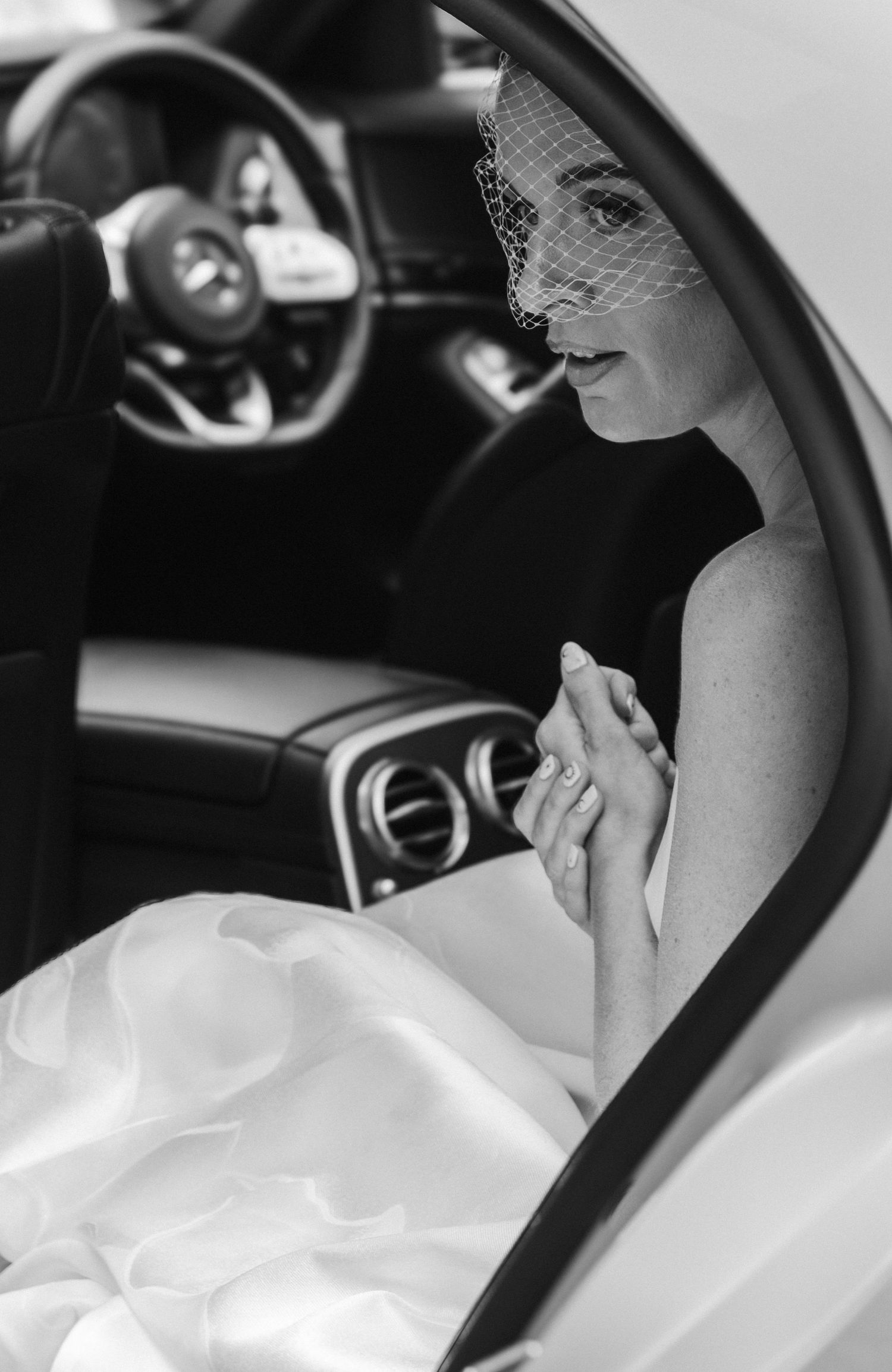 Black and white photo of a bride sitting in a luxury car.