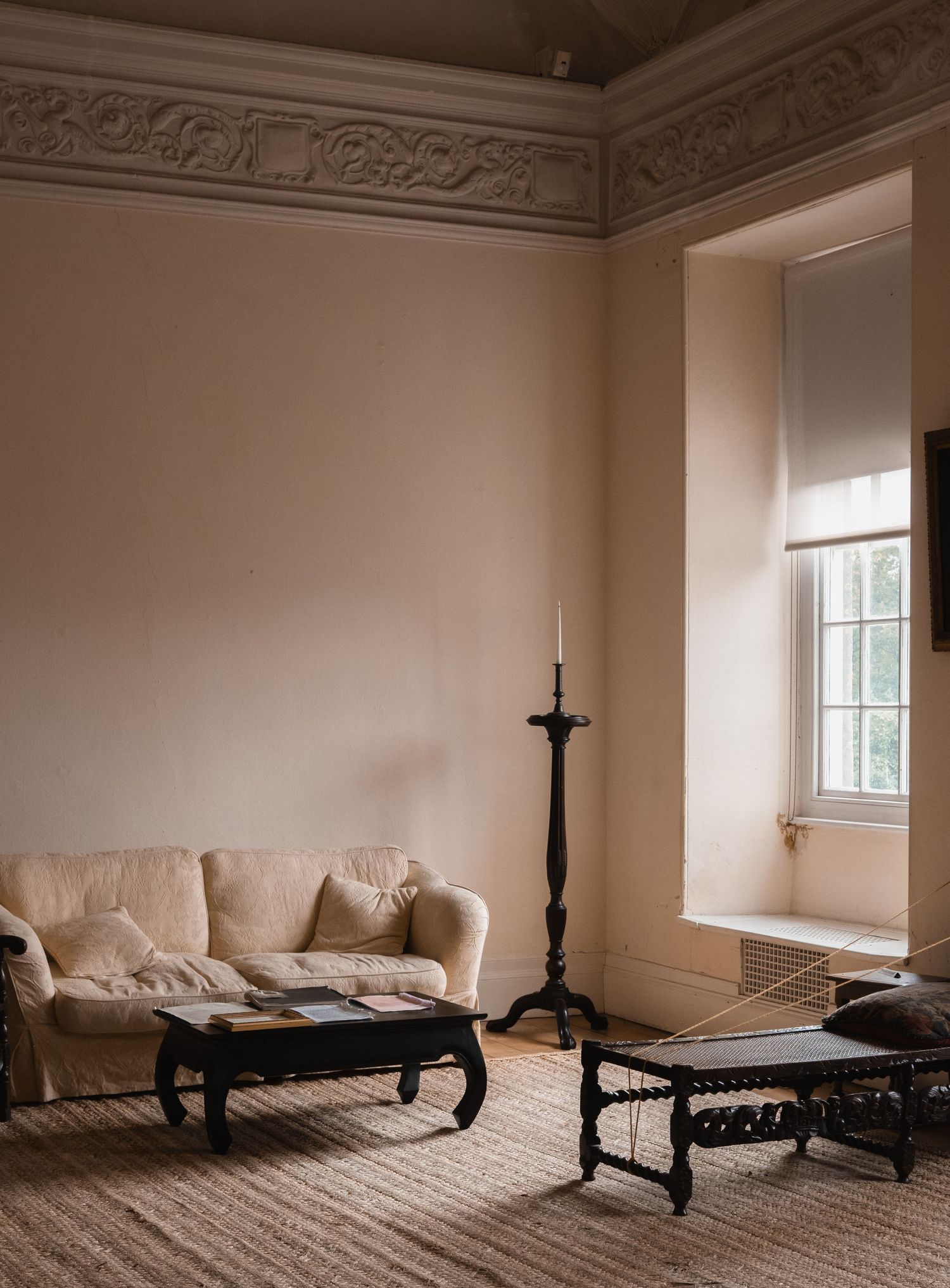 Elegant period room with cream walls, ornate molding, and vintage furniture in soft lighting.