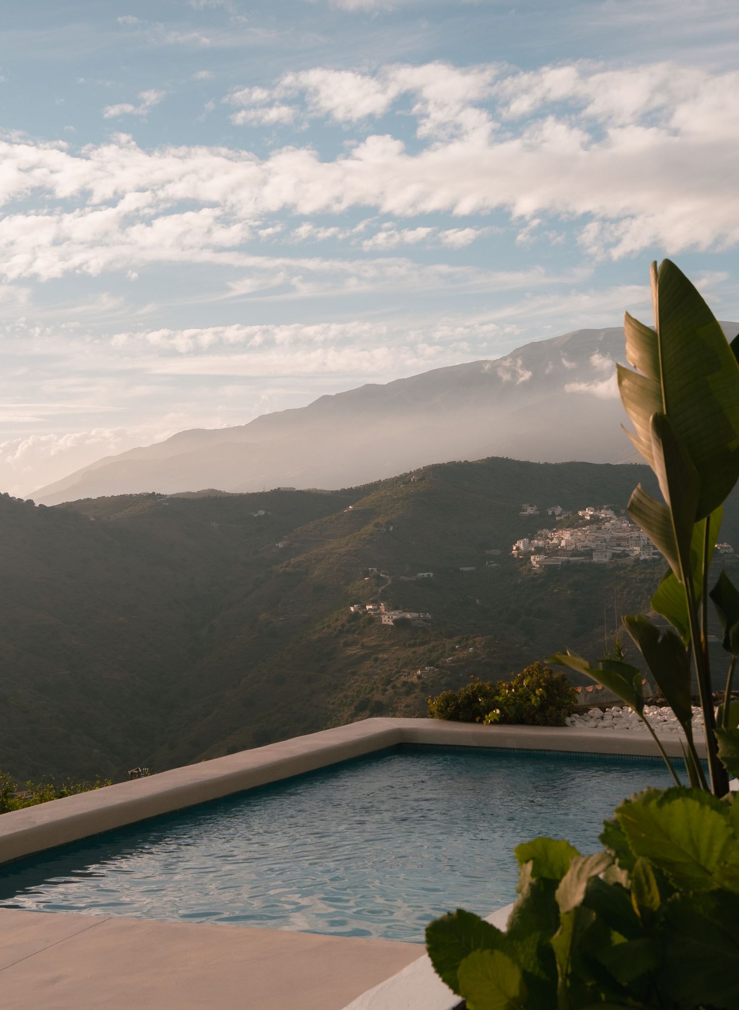 Infinity pool with stunning mountain views, lush tropical plants, and a dramatic cloudy sky at golden hour.