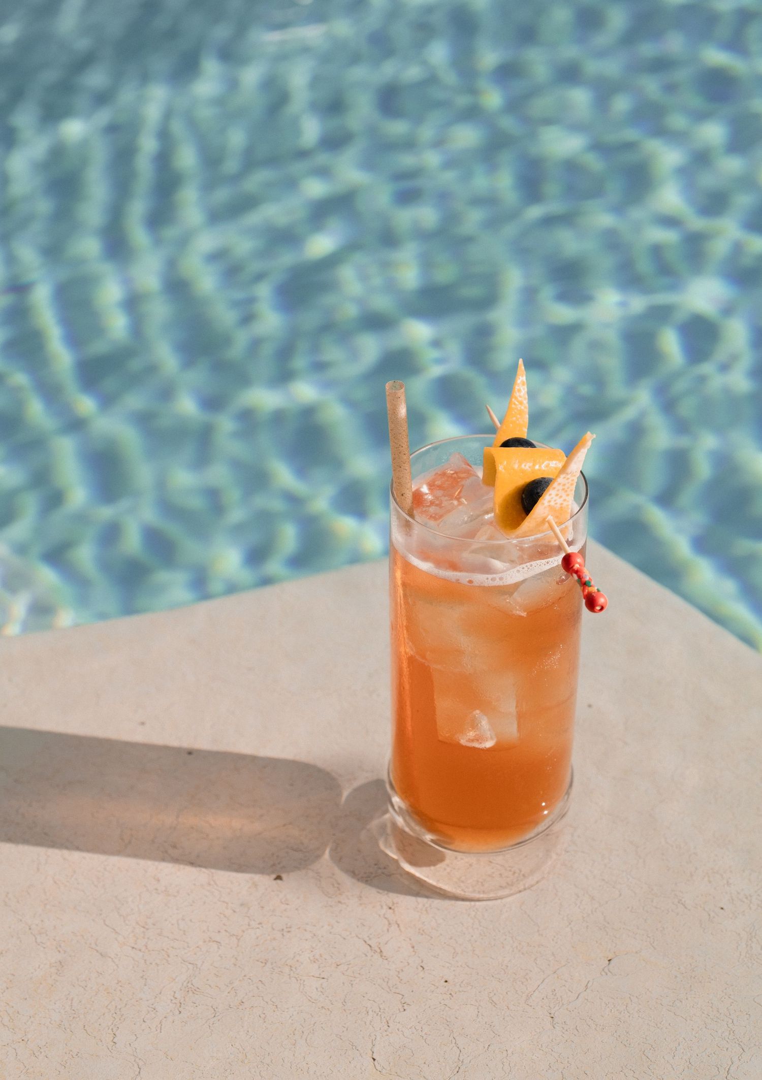A tropical cocktail garnished with pineapple and umbrella sits poolside on a sunny day.