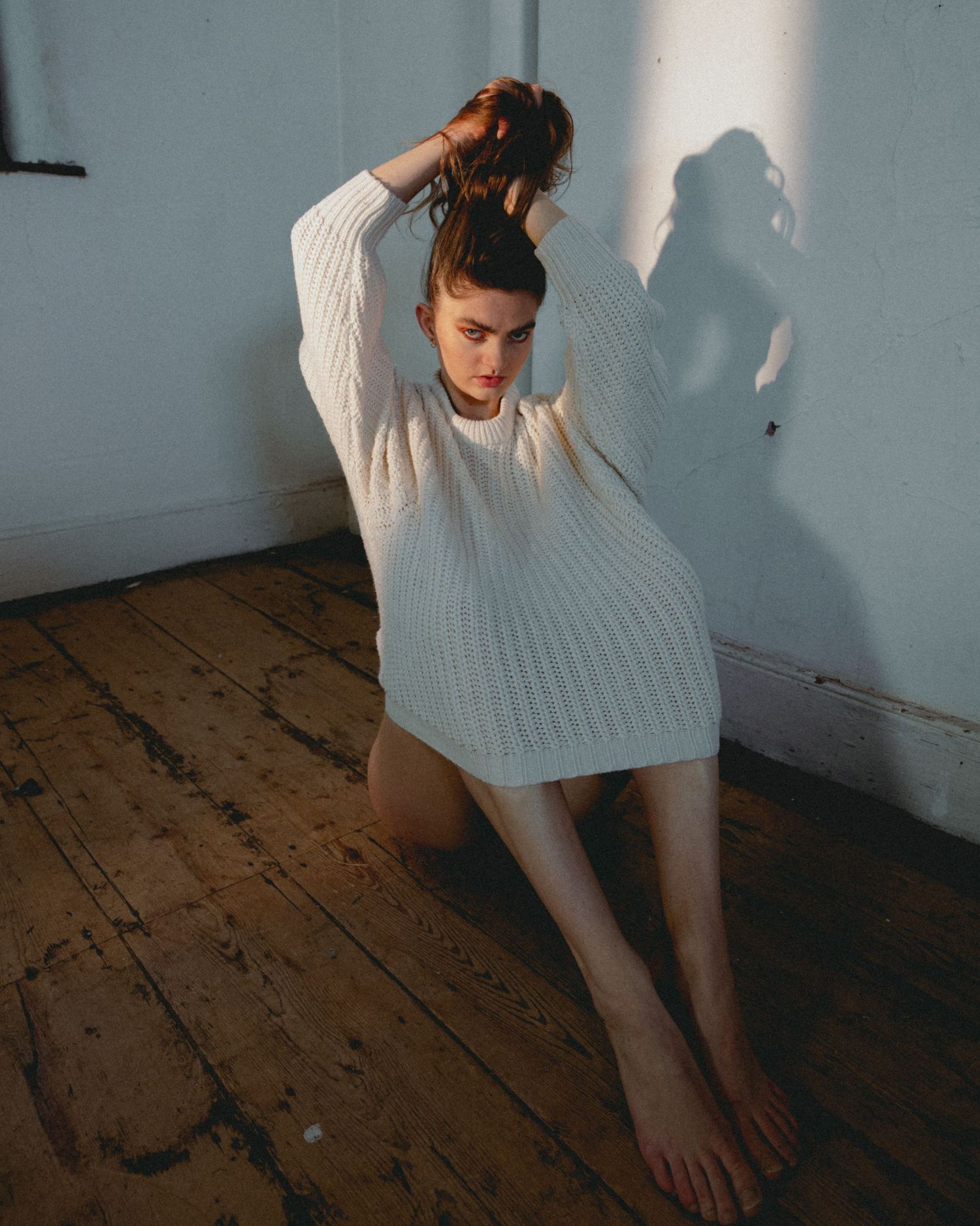 Figure in white sweater moves gracefully against blue wall and wooden floor.