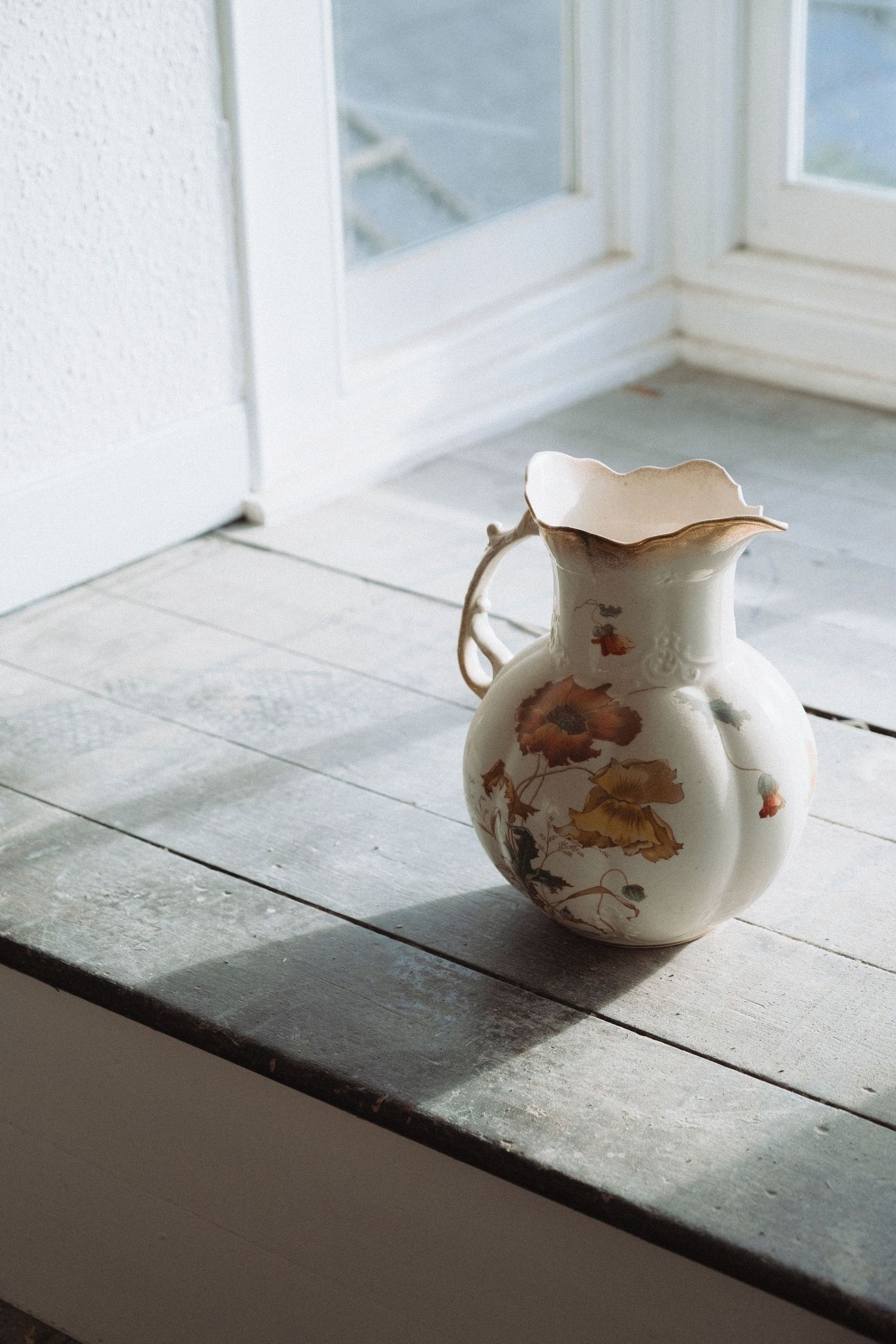 Vintage floral porcelain pitcher sitting on white windowsill in natural light.