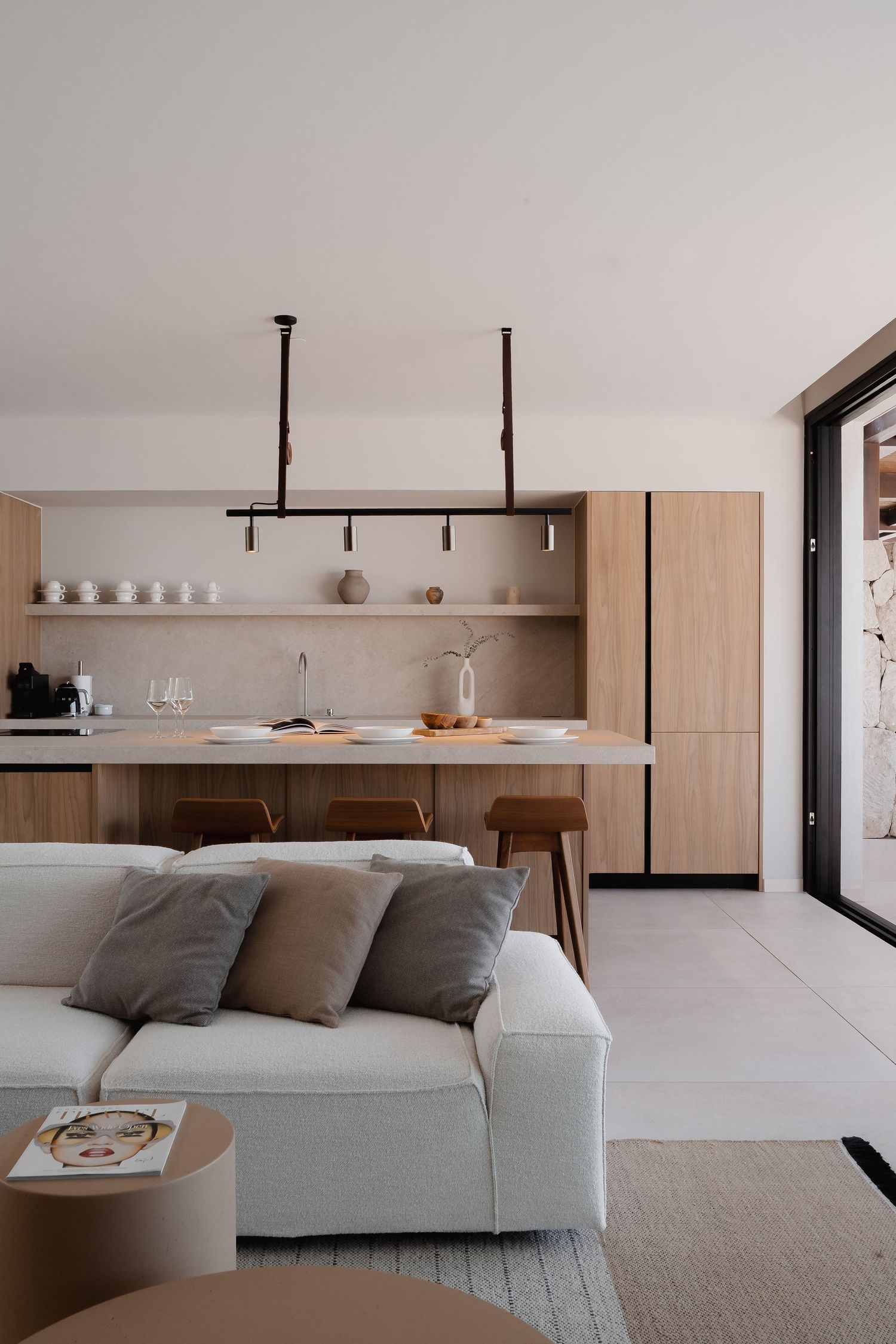 Modern open-plan kitchen and living room with warm wood cabinetry, white sofa, and minimalist pendant lighting.