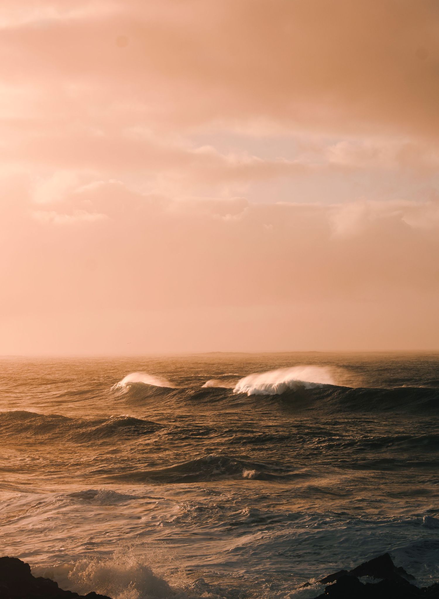 Dramatic seascape with rolling waves under a warm orange sunset sky.