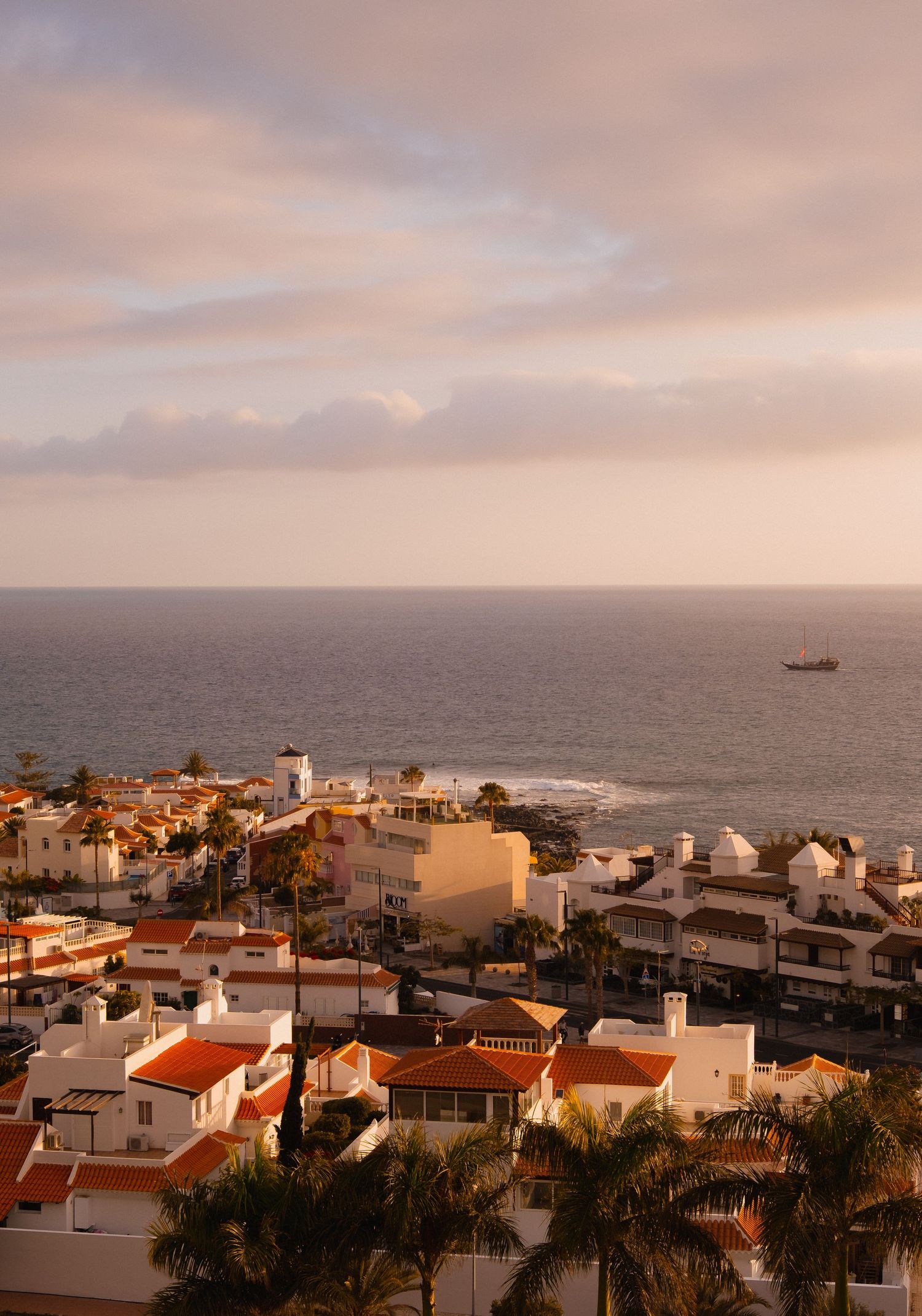 Aerial view of a coastal Mediterranean town with white buildings and terracotta roofs at golden sunset hour.