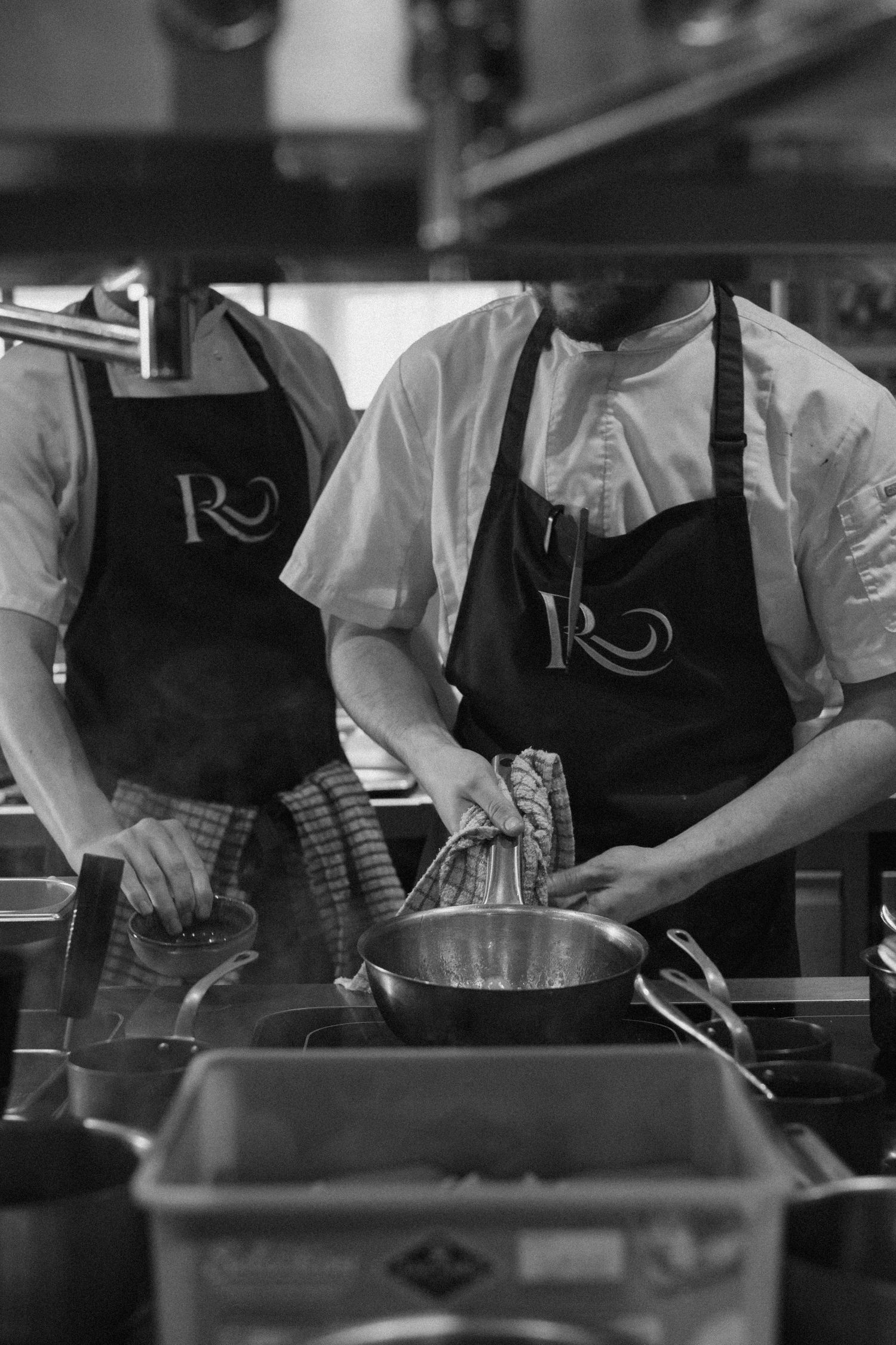 Restaurant kitchen staff preparing food in a commercial kitchen wearing white chef coats and dark aprons.