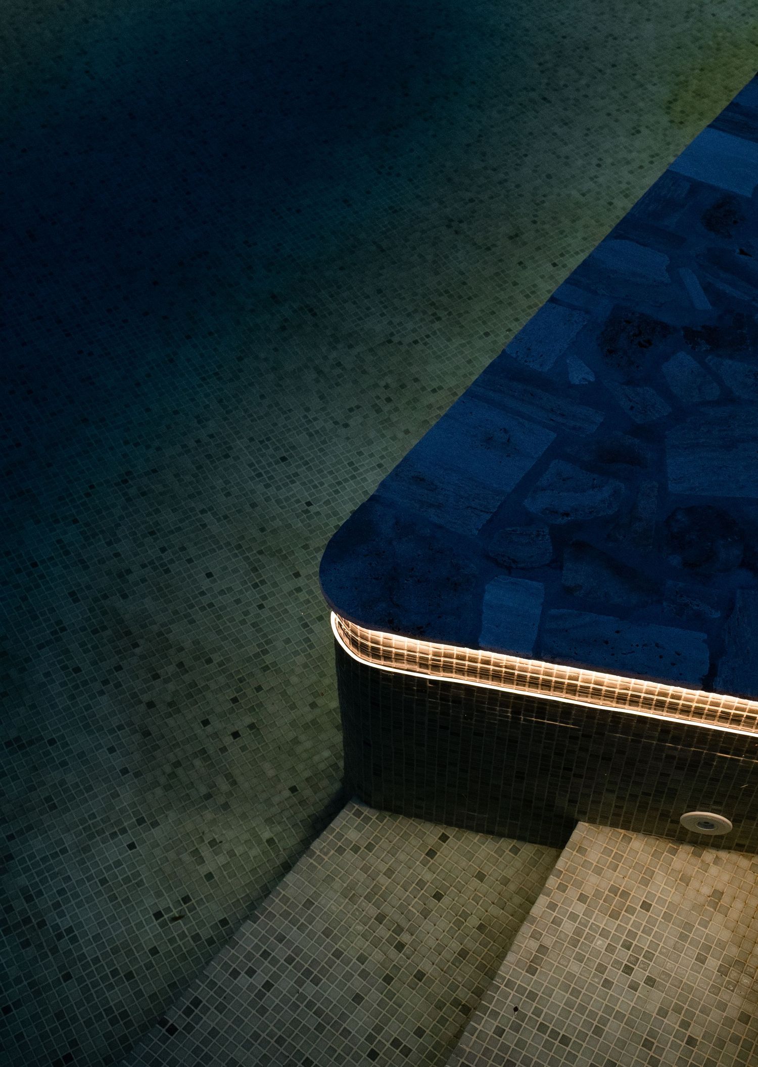 Modern pool edge with mosaic tile detail and curved border in low light.