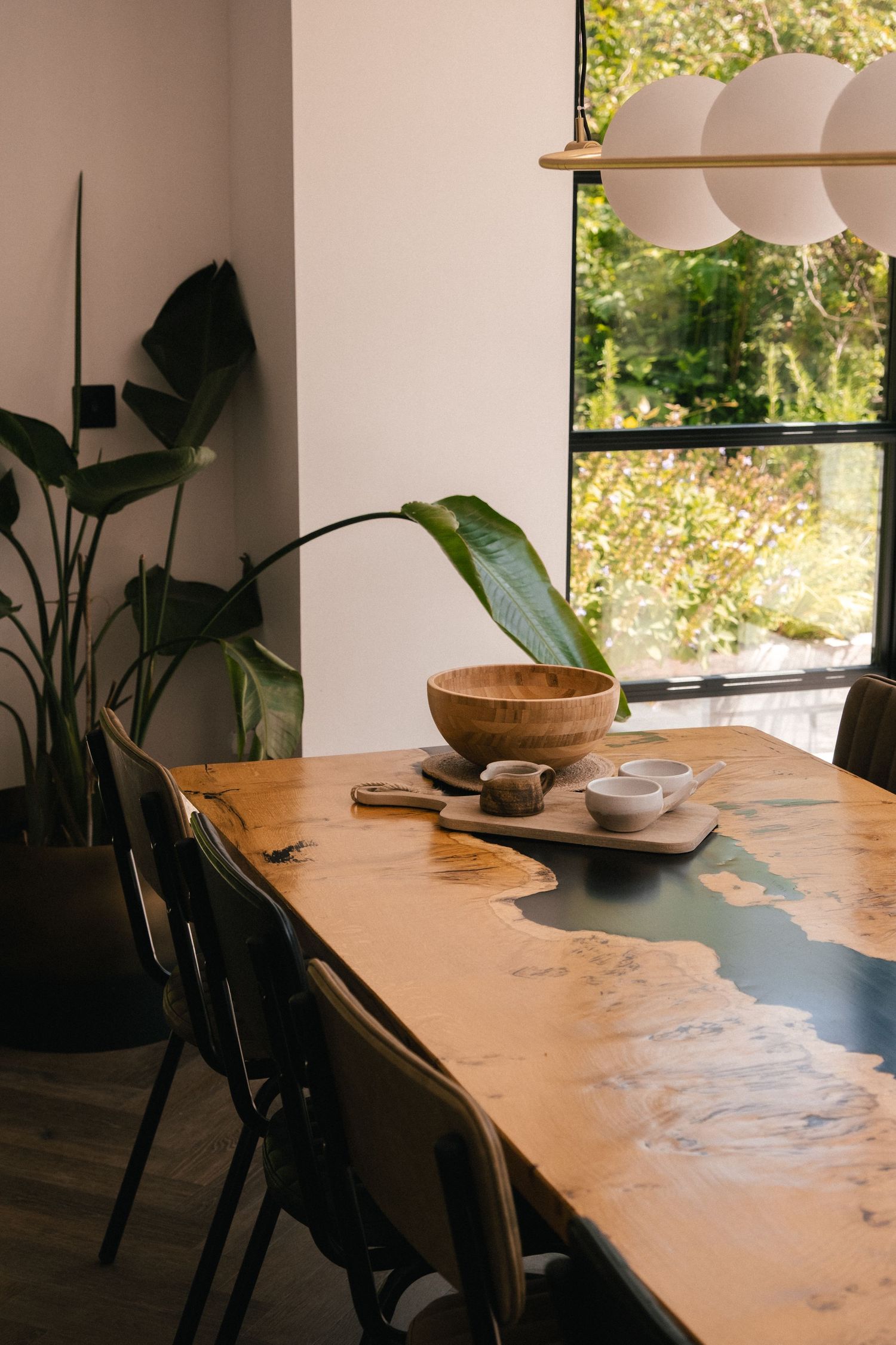 Modern dining room with live edge wooden table, pendant lights, and large windows bringing in natural light.