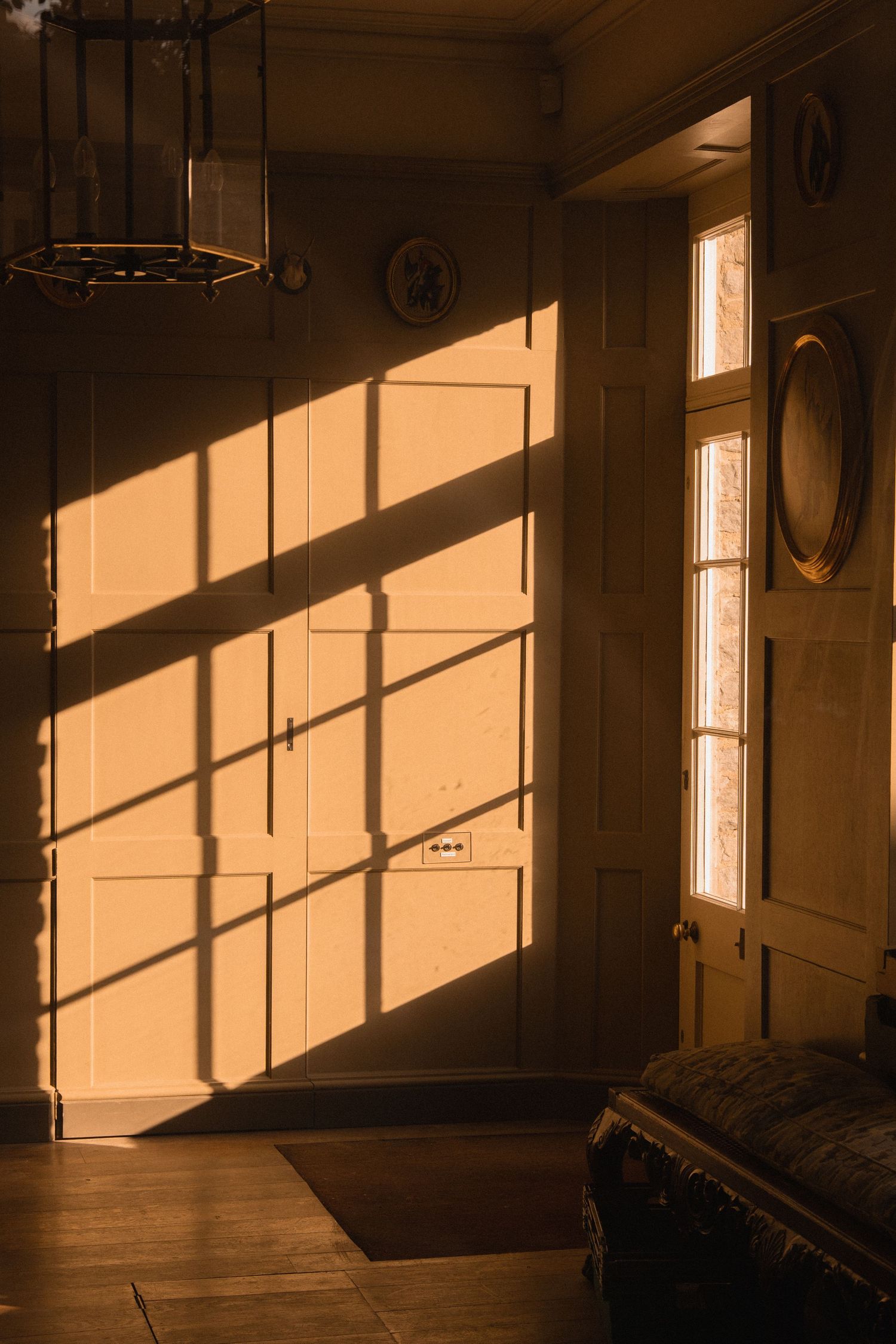 Warm golden sunlight casting geometric shadows through a window onto a classic interior door and wooden floor.