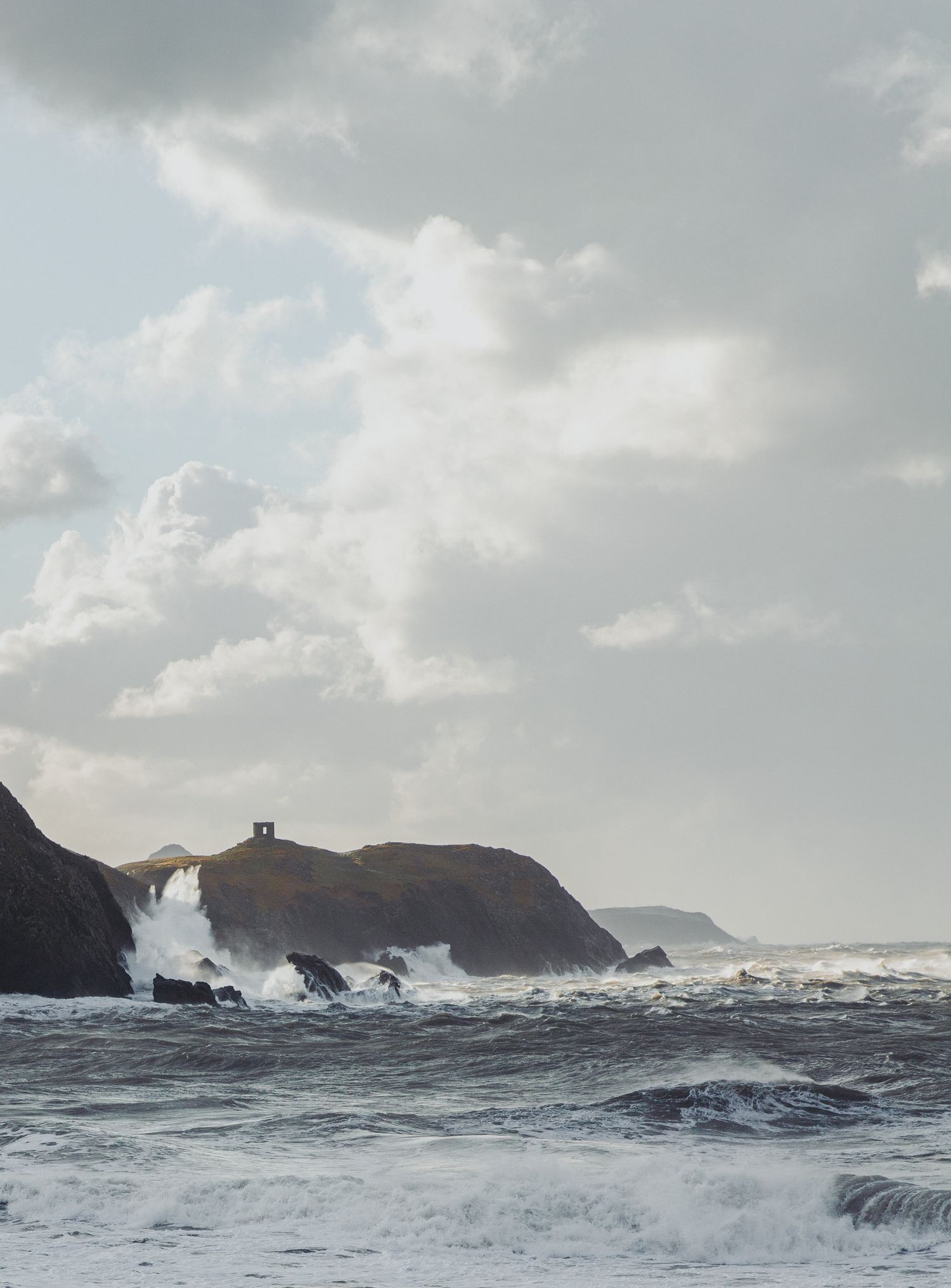 Dramatic seascape with crashing waves against rocky cliffs under cloudy sky.