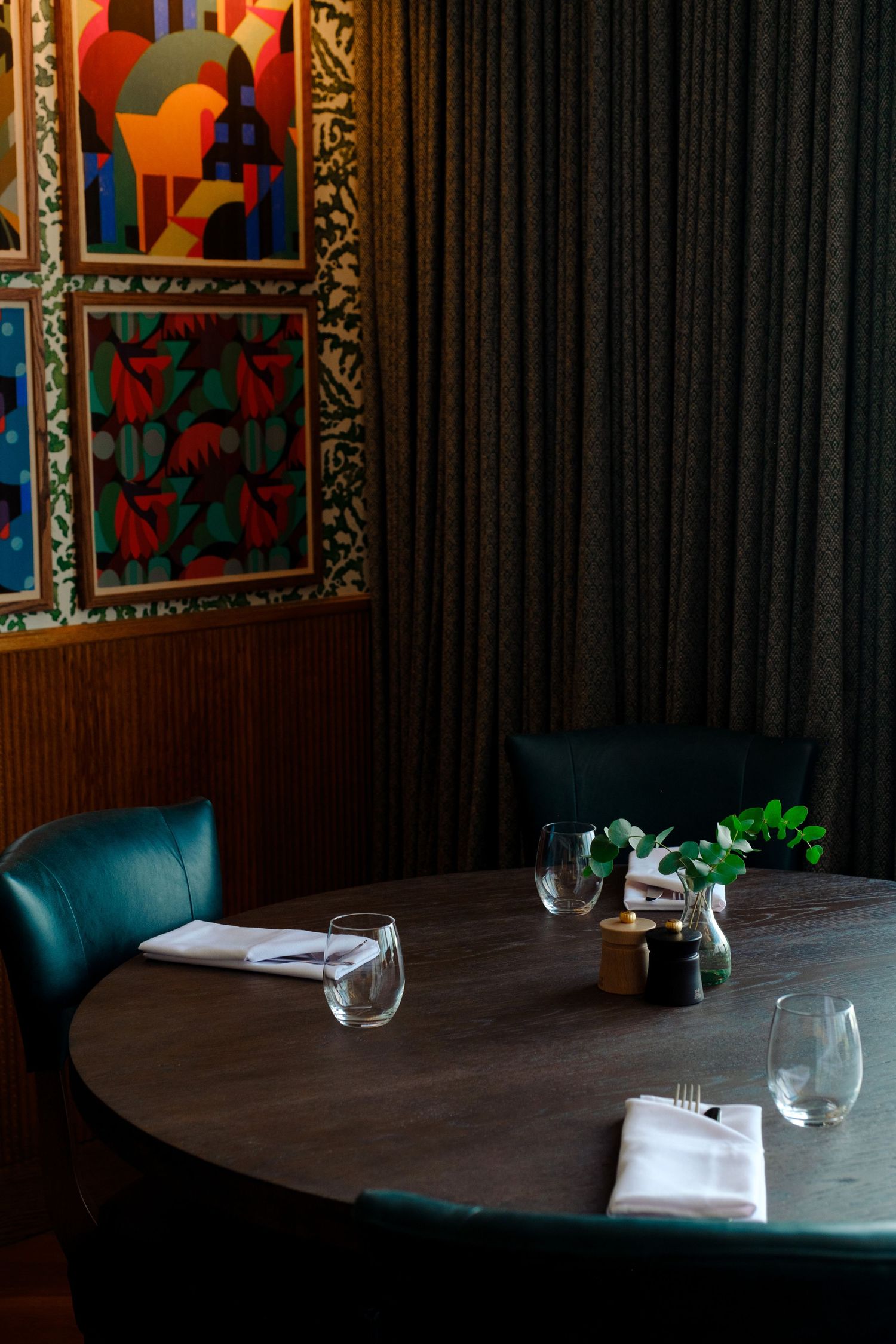 Elegant restaurant table setting with dark leather chairs and colorful geometric artwork on wall.