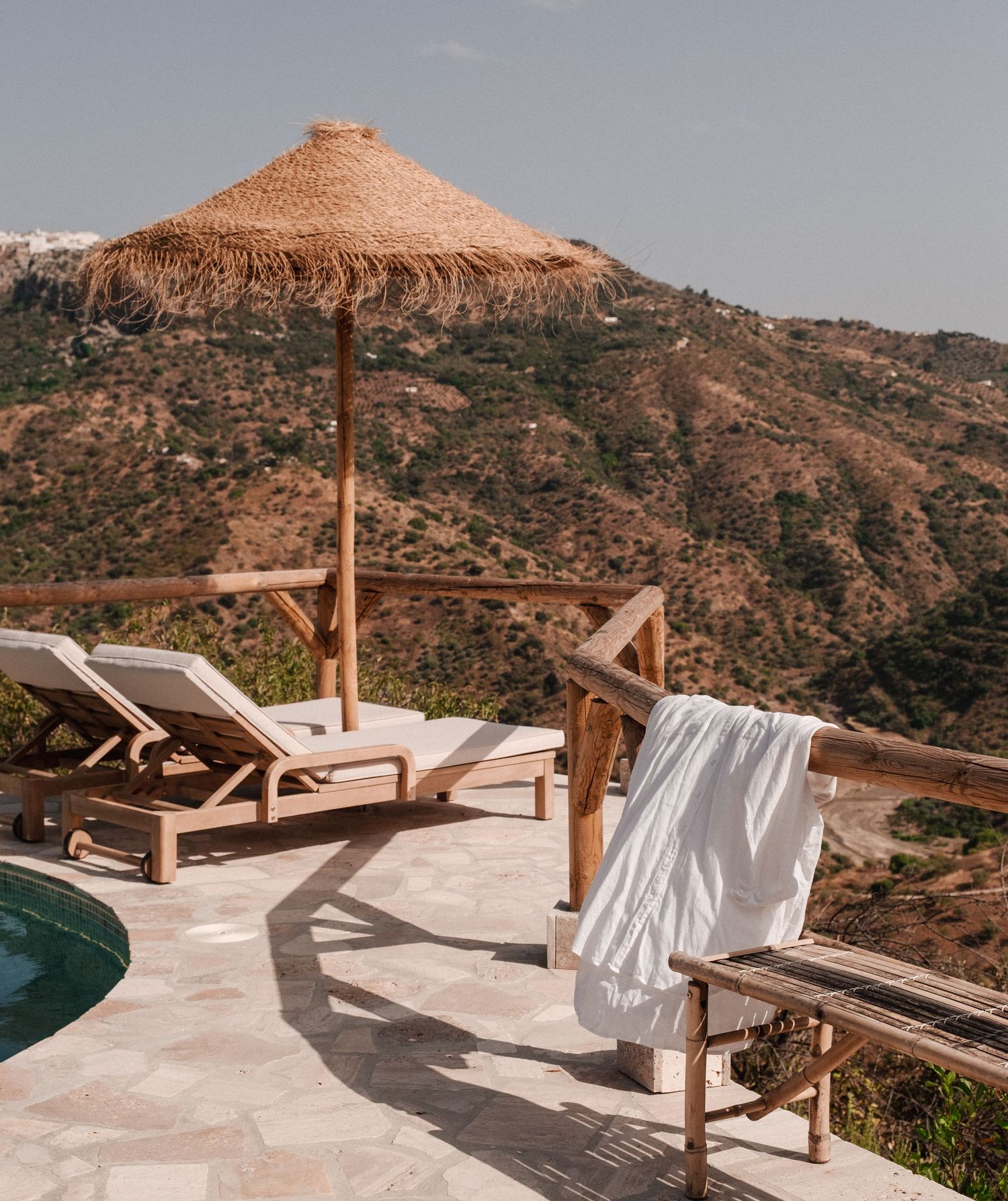 Luxurious outdoor lounge area with white cushioned beds overlooking mountainous terrain.