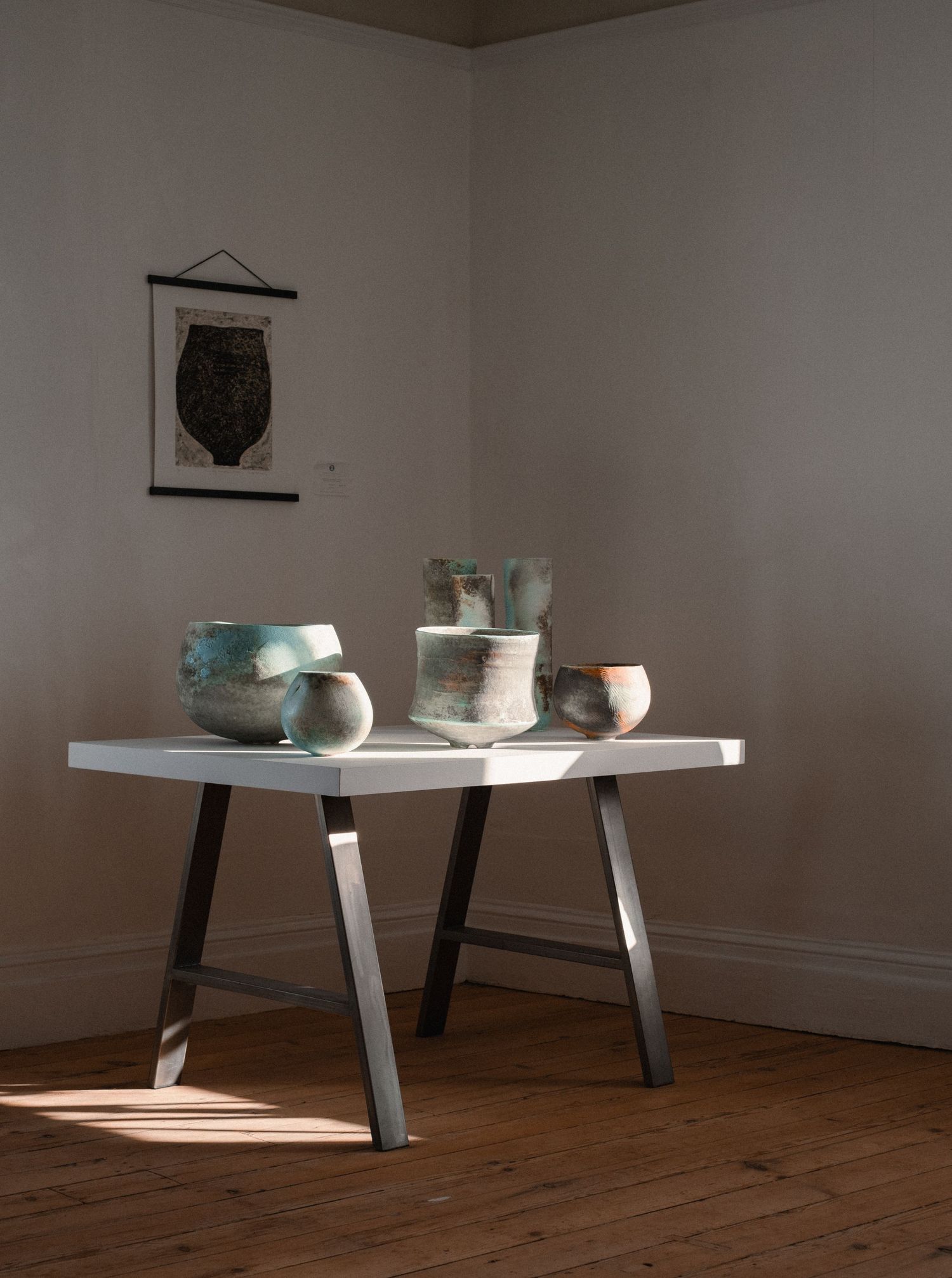 Minimalist white table display with ceramic pieces in a gallery-like setting.