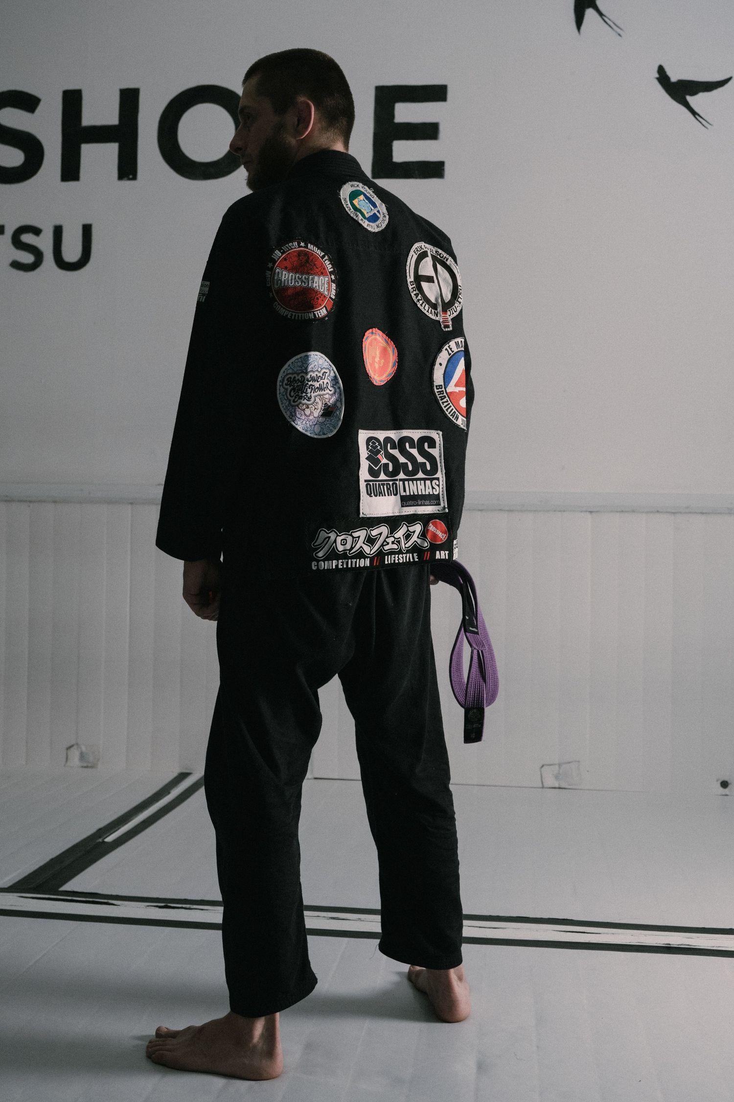 Lower body view of martial arts practitioners wearing black uniforms with patches training in a bright studio space.