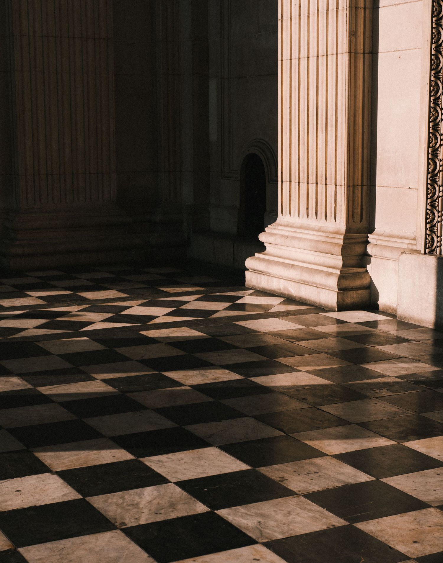 Classic checkerboard marble floor with white columns casting dramatic shadows.