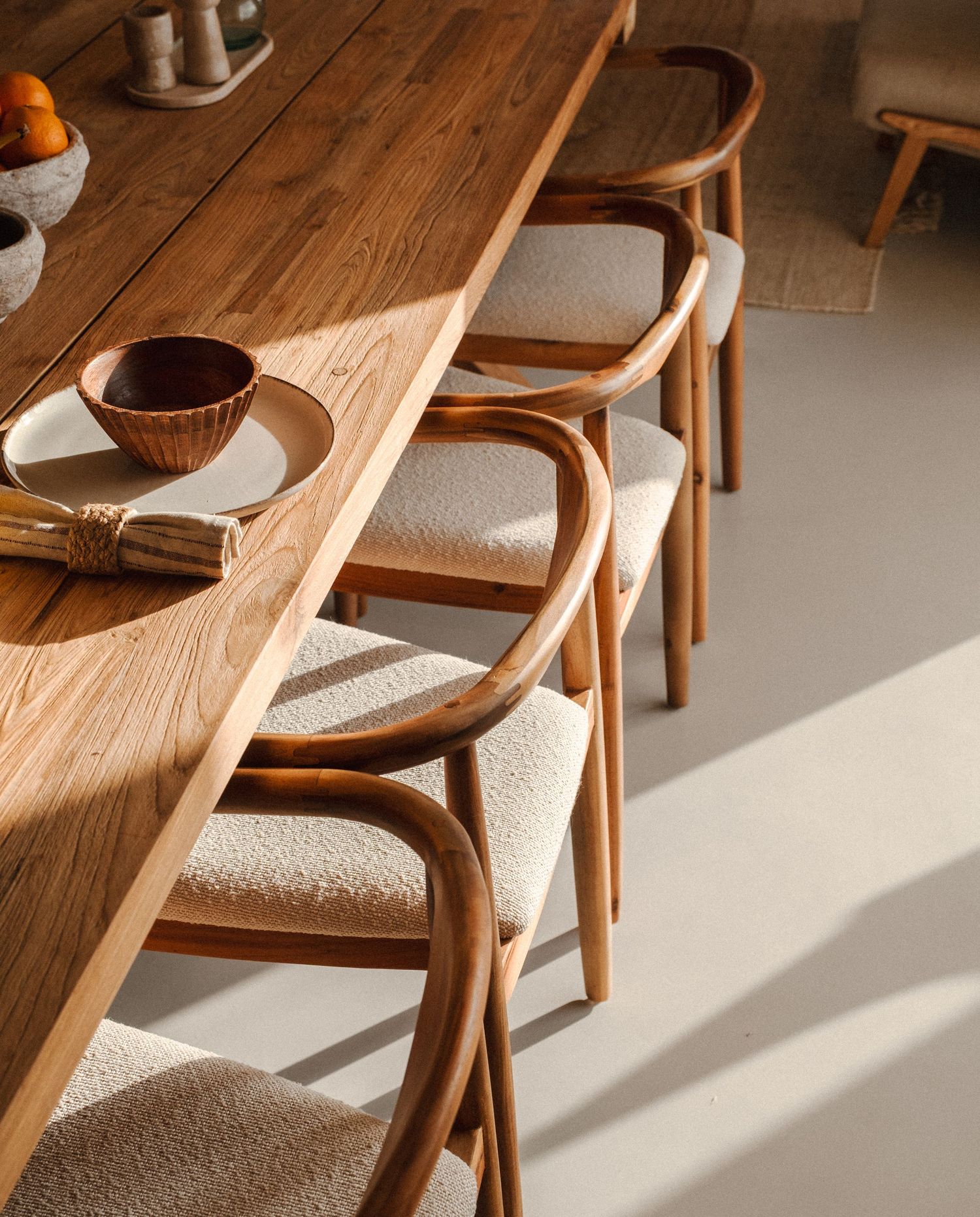 Wooden dining chairs with textured upholstery casting dramatic shadows in natural light.