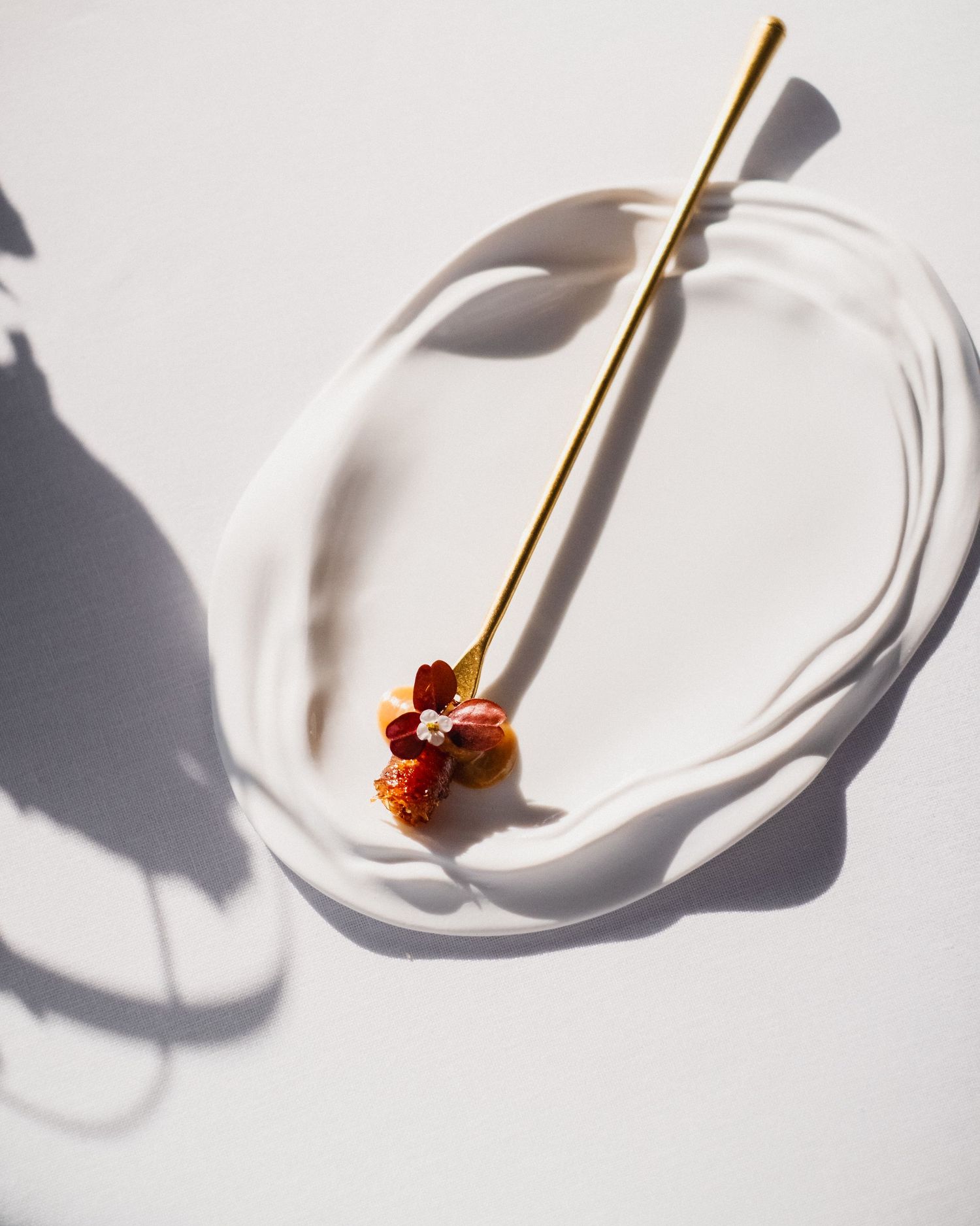 Gold hair pin with red and orange dried flowers on a white ceramic dish casting elegant shadows.