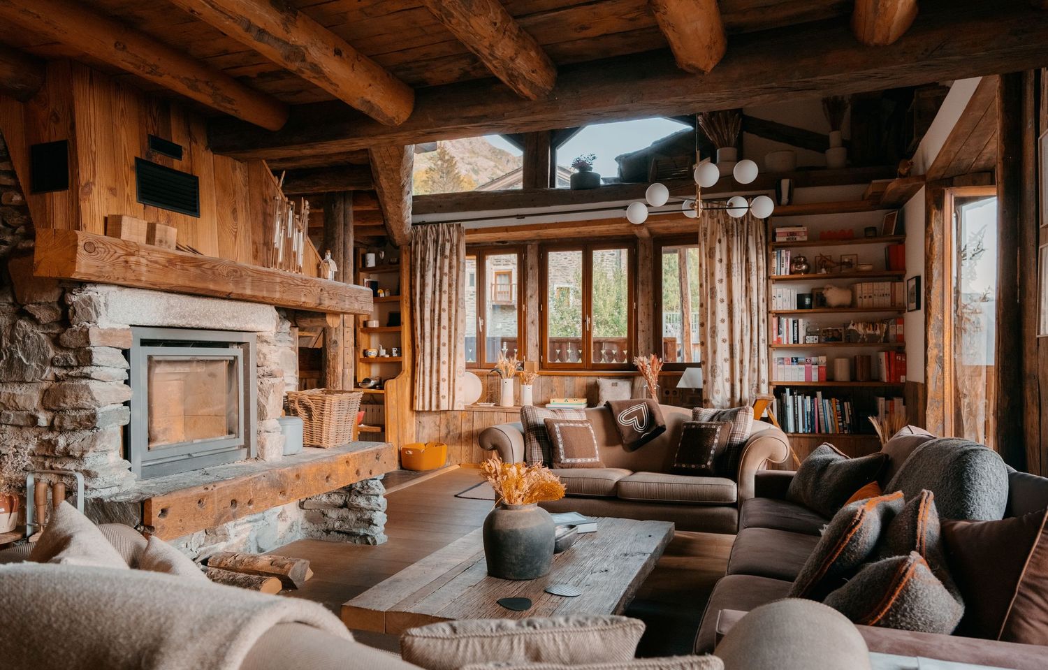 Cozy rustic log cabin living room with stone fireplace, wooden beams, plush sofas, and warm ambient lighting.