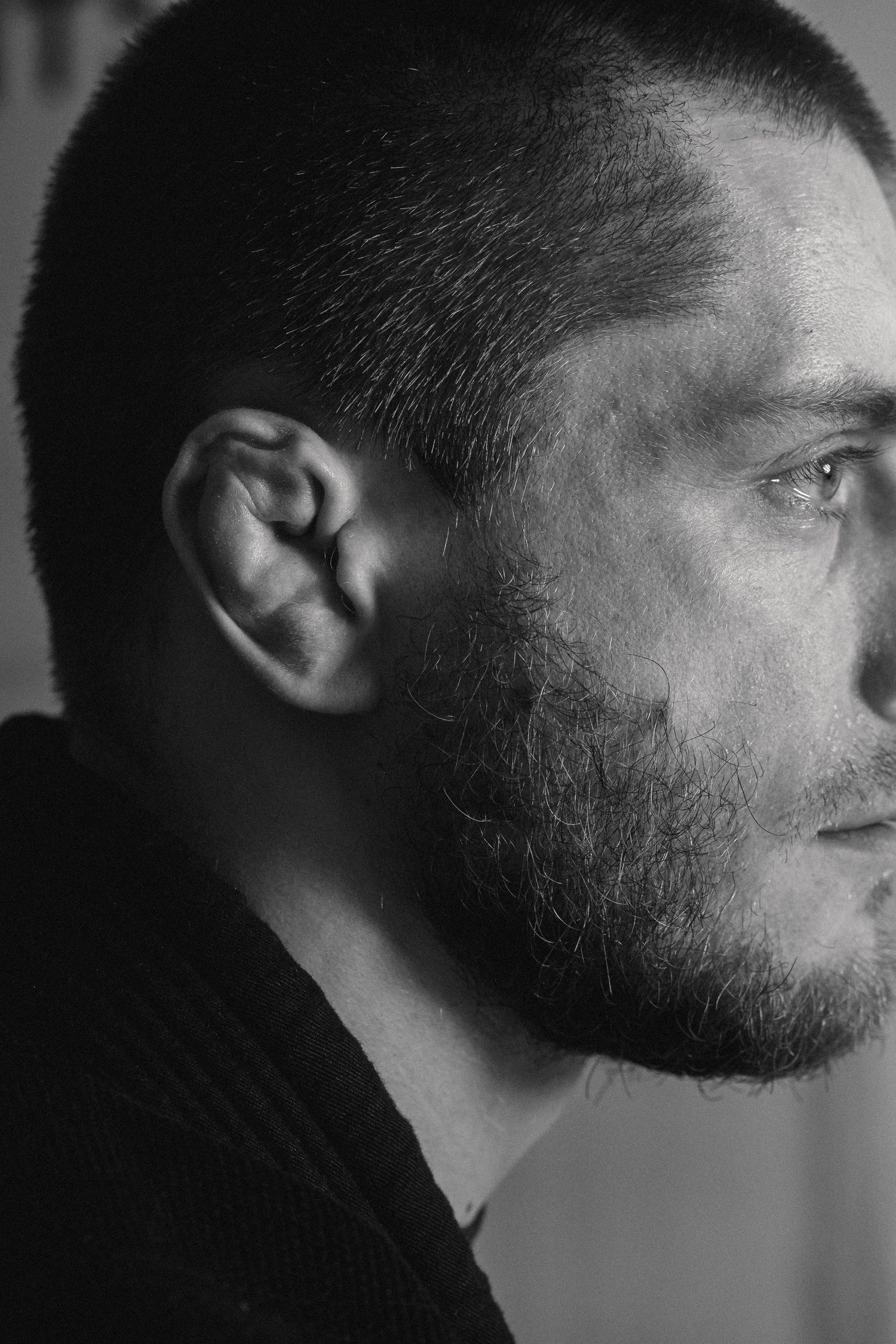 Black and white profile portrait showing a bearded man with short hair in dramatic side lighting.