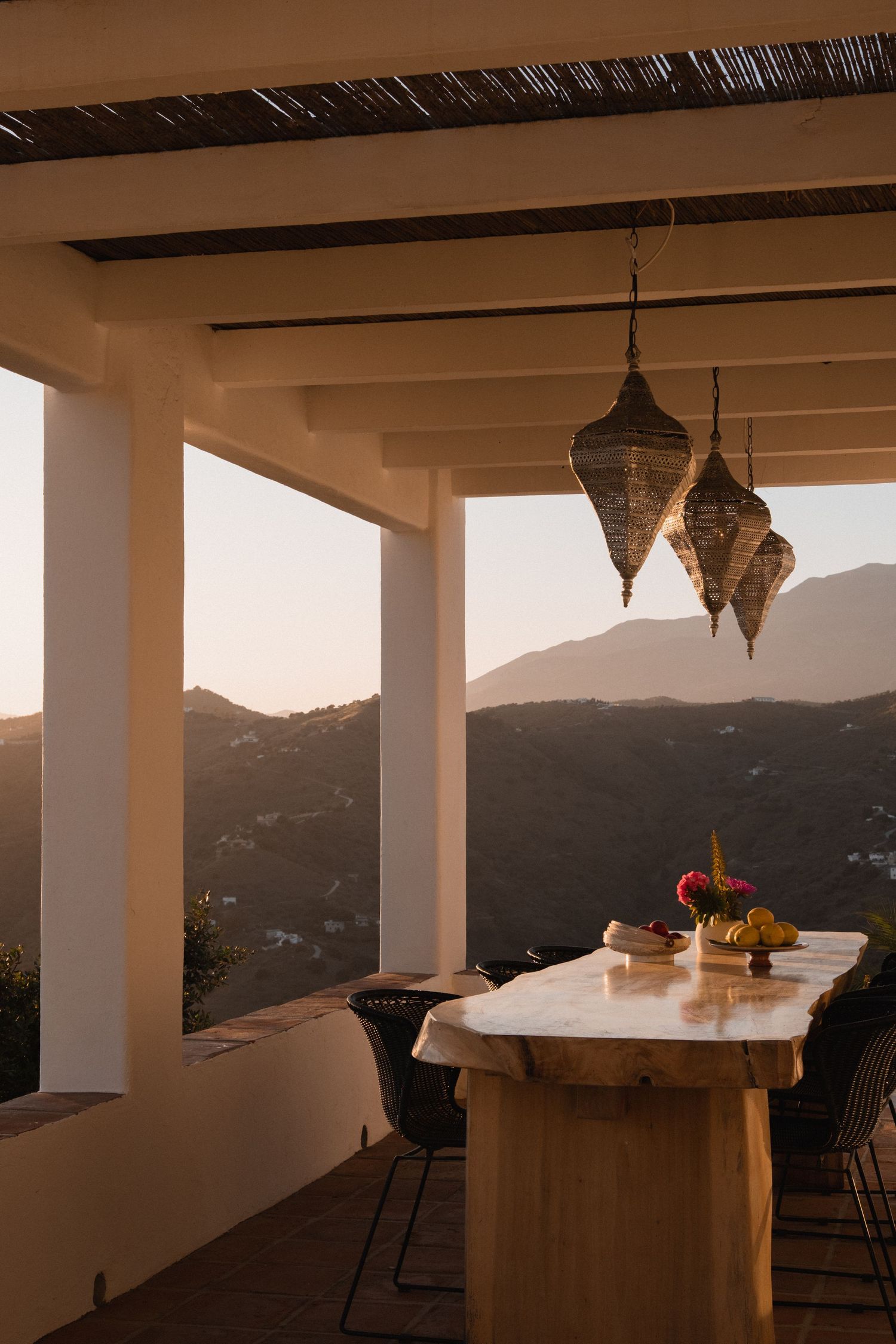 Rustic outdoor terrace with Moroccan lanterns, marble table, and mountain sunset views.