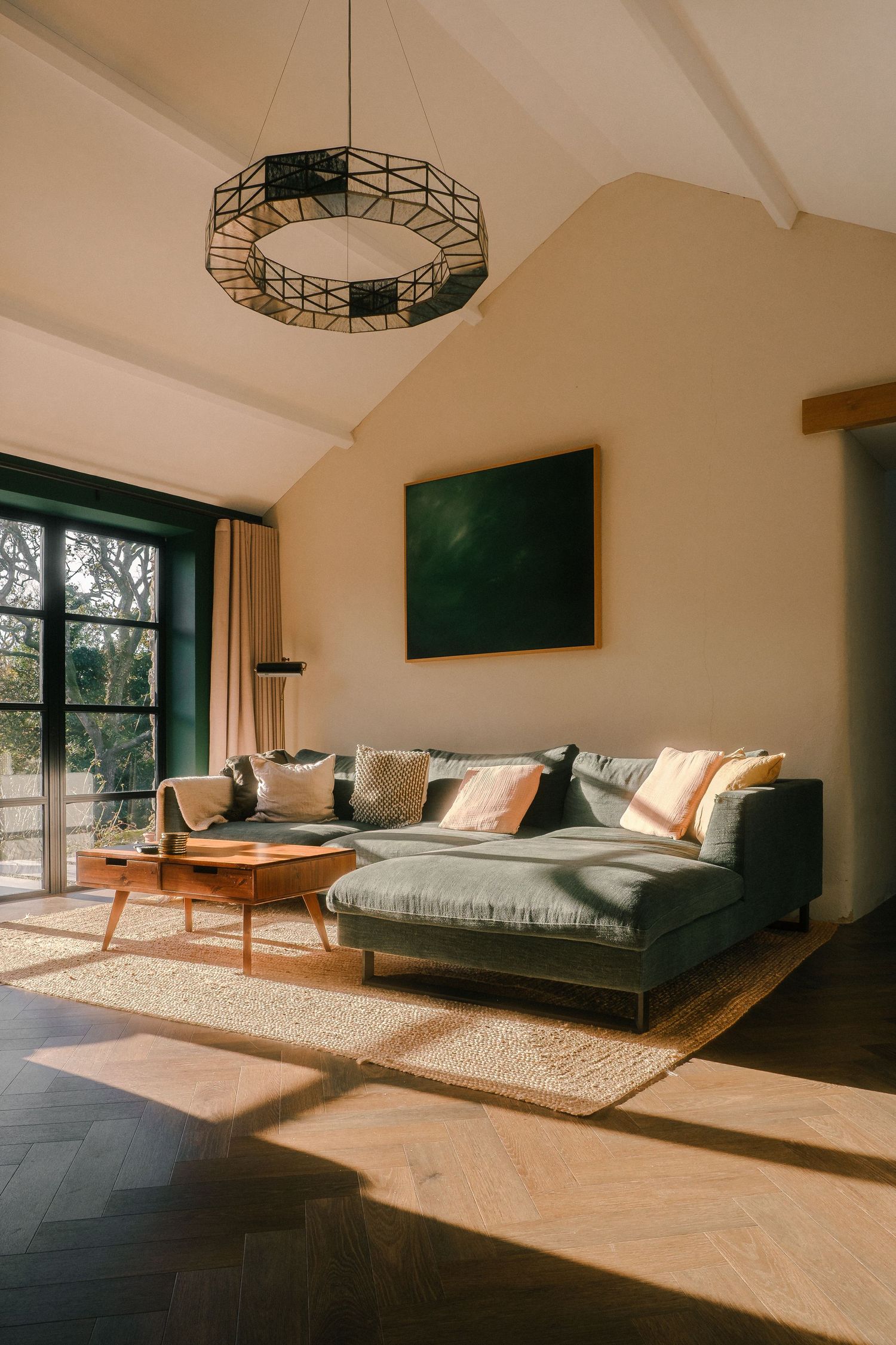 Modern living room with gray sectional sofa and wooden coffee table bathed in natural sunlight through large windows.
