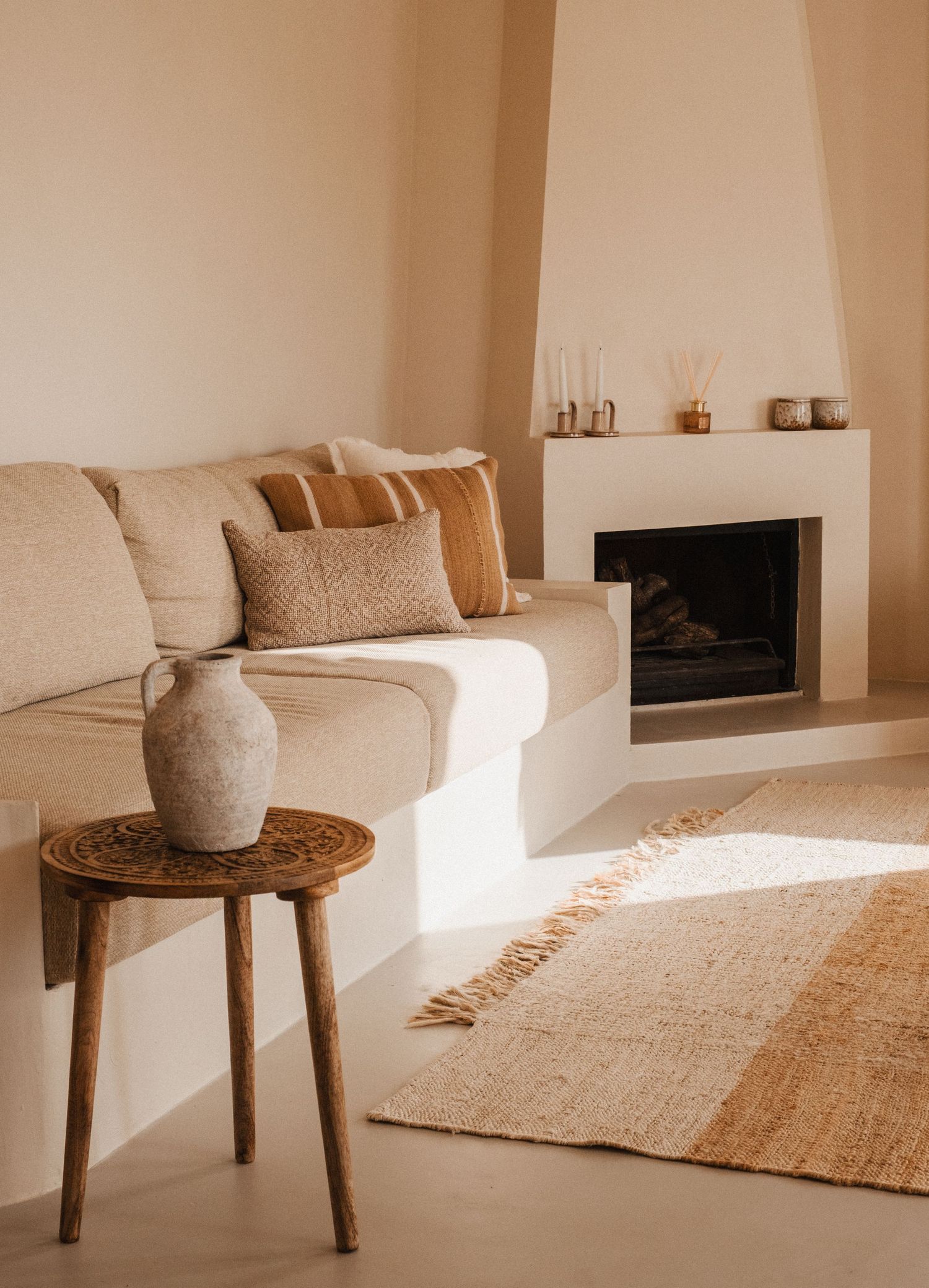 Minimalist living room with beige couch, wooden side table, and modern fireplace in warm tones.