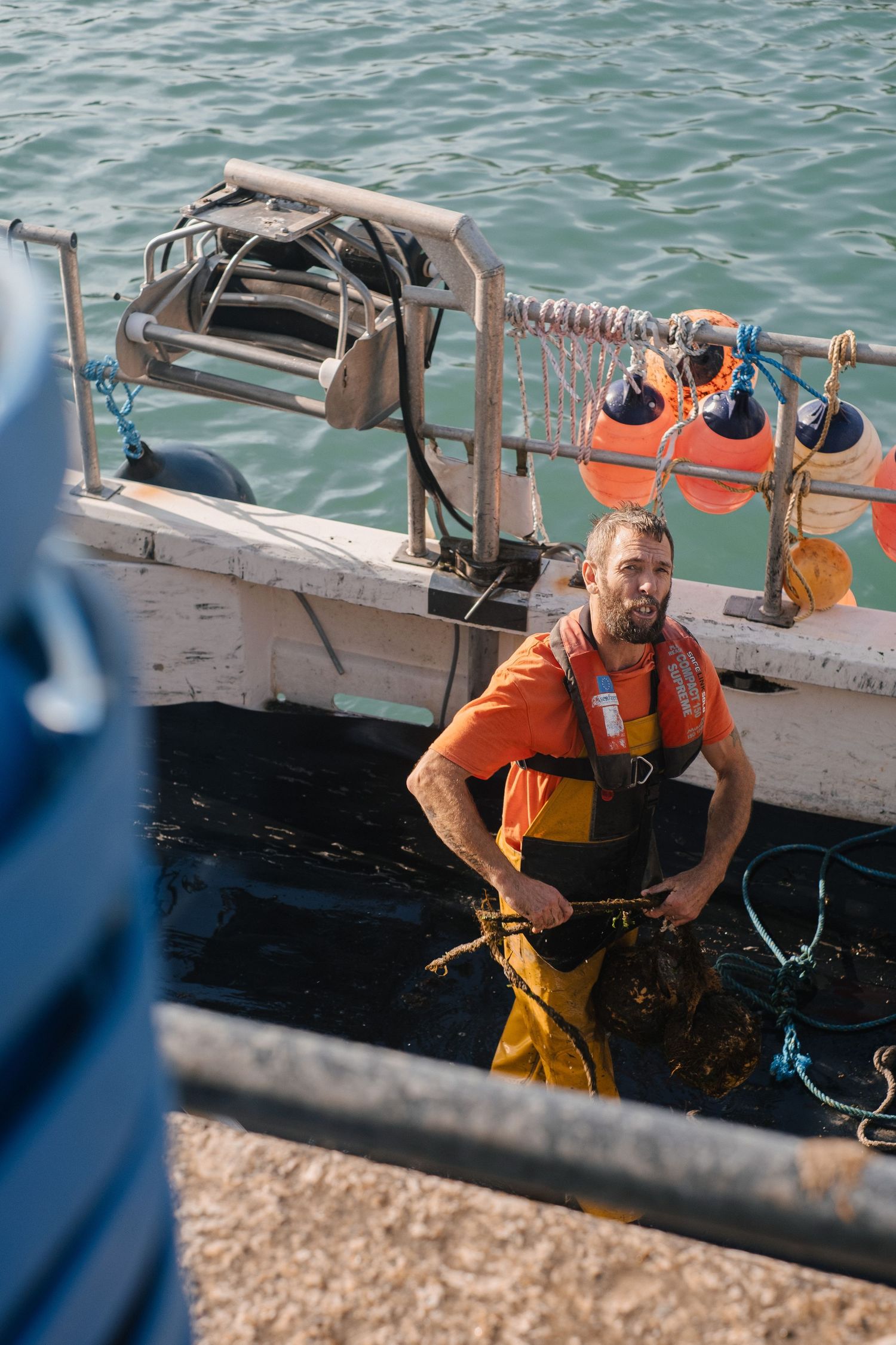 Fisherman in orange safety gear working on a boat deck.
