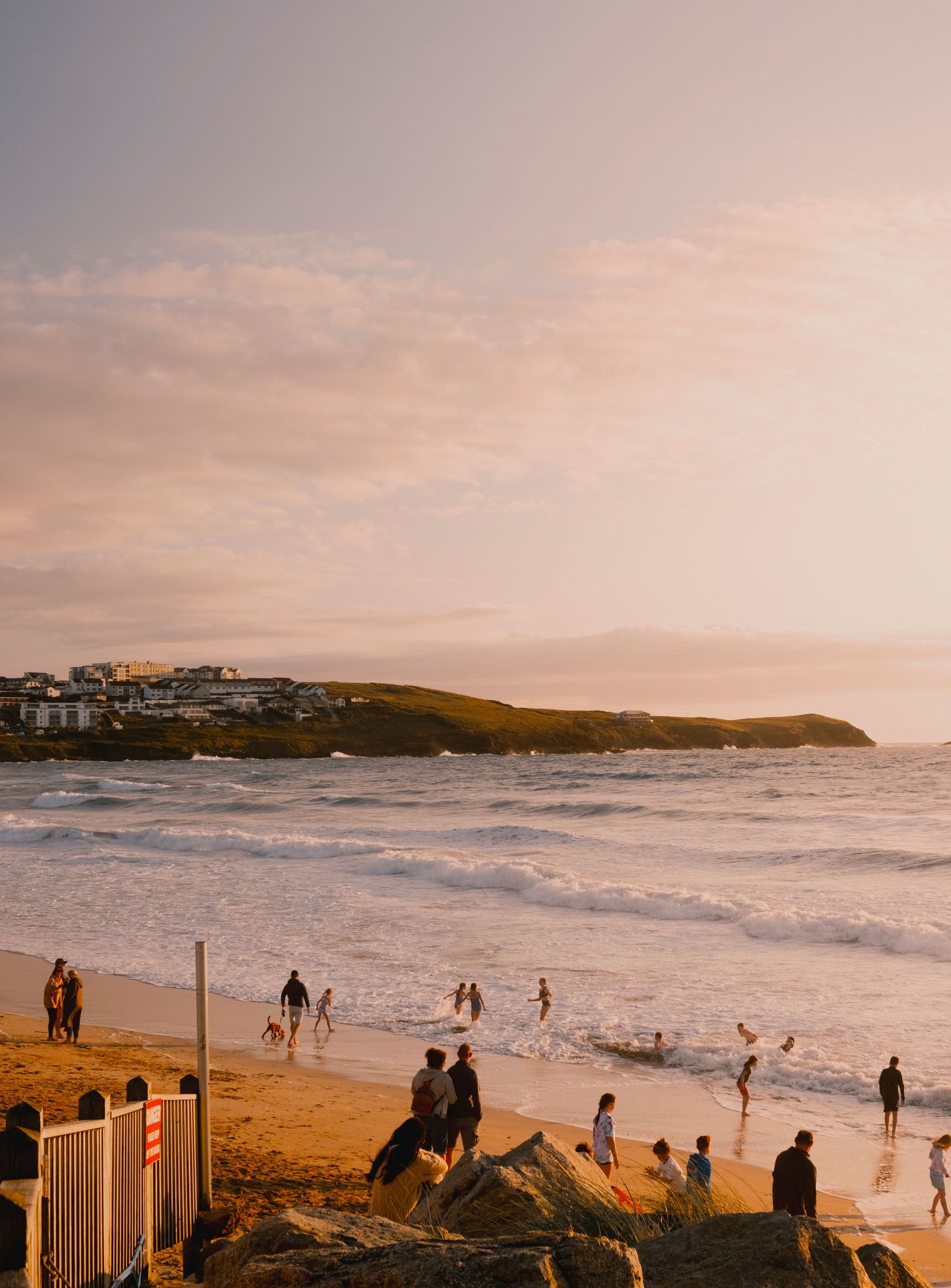 Coastal beach scene at sunset with people gathering along the shoreline.