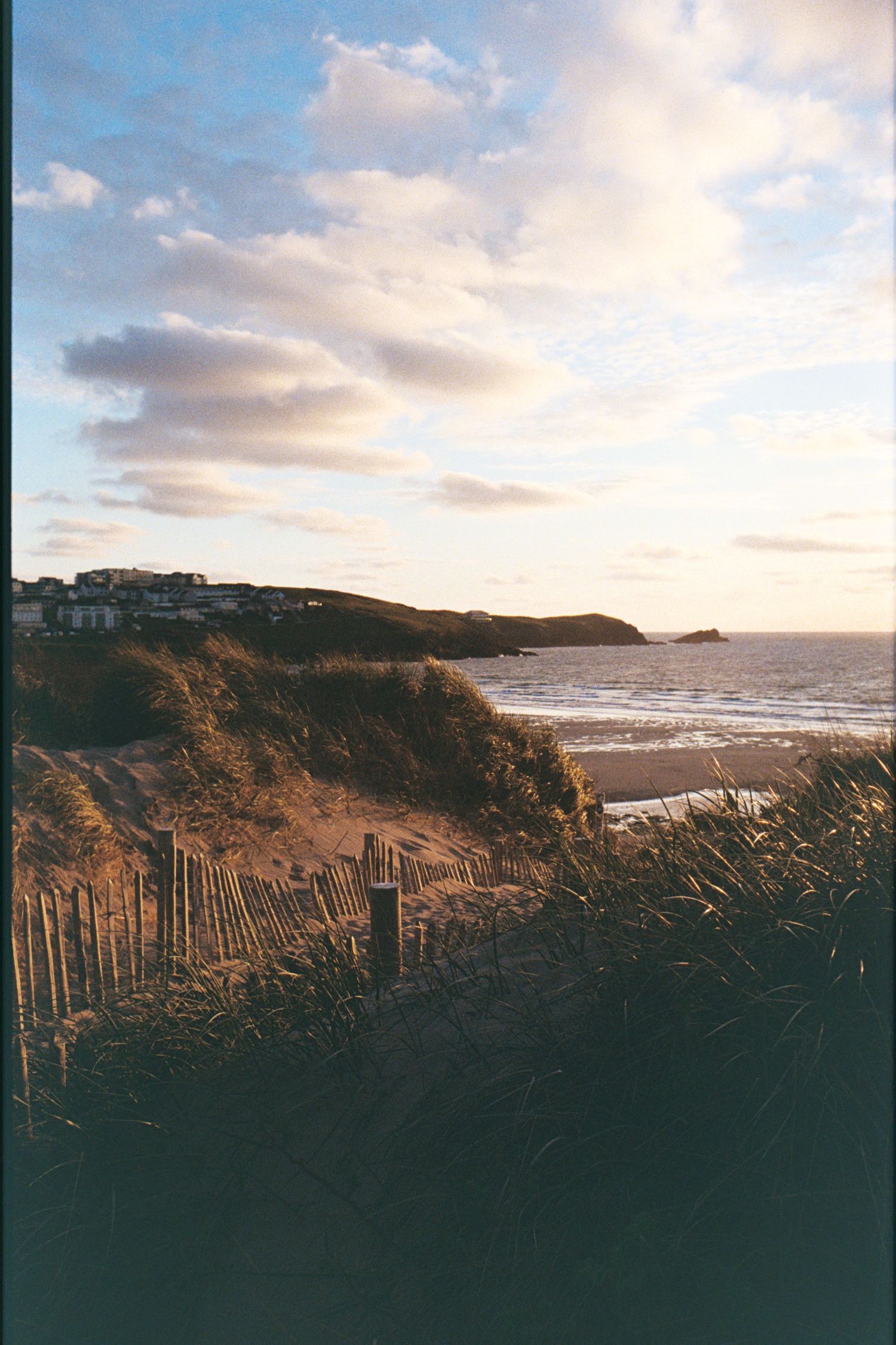 Coastal sunset landscape with wooden fence silhouetted against dramatic cloudy sky.